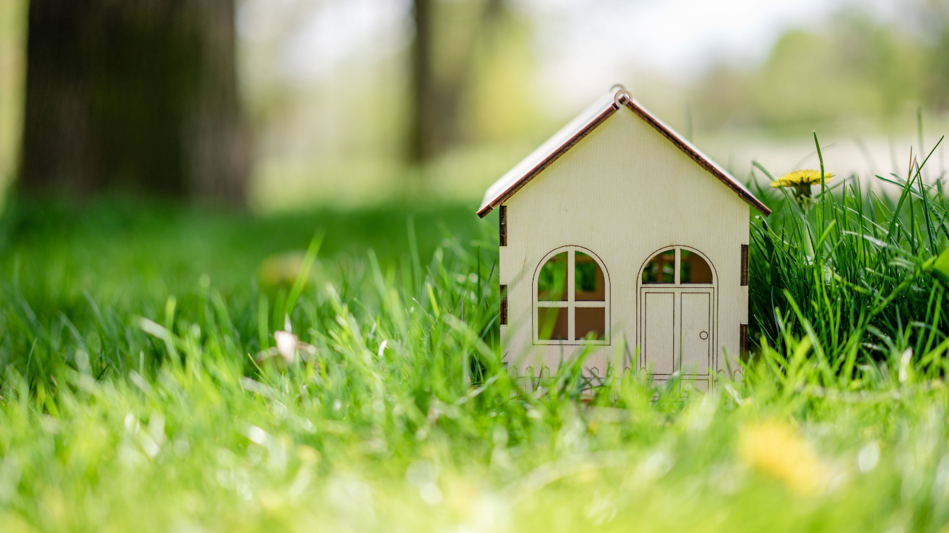 Small wooden house model in green grass symbolizing ADU.