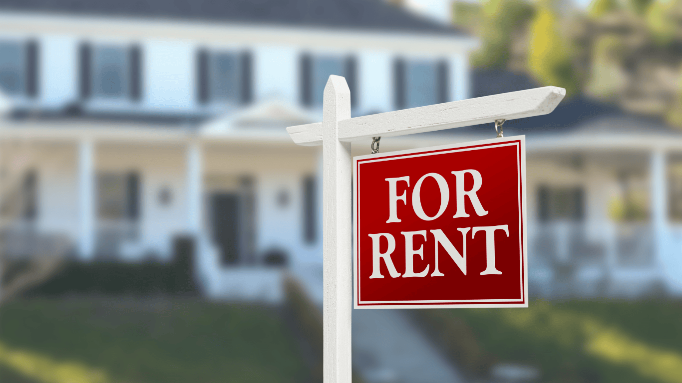 Red ‘For Rent’ sign in front of a suburban white house with black shutters — representing rental property investment and house hacking opportunities.