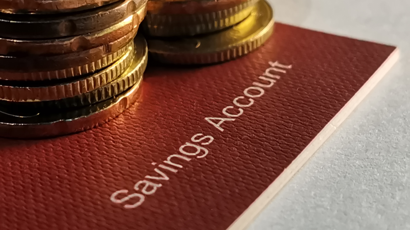 Stack of gold coins placed on a red savings account booklet, symbolizing personal finance, banking, and the importance of investing beyond traditional savings accounts.