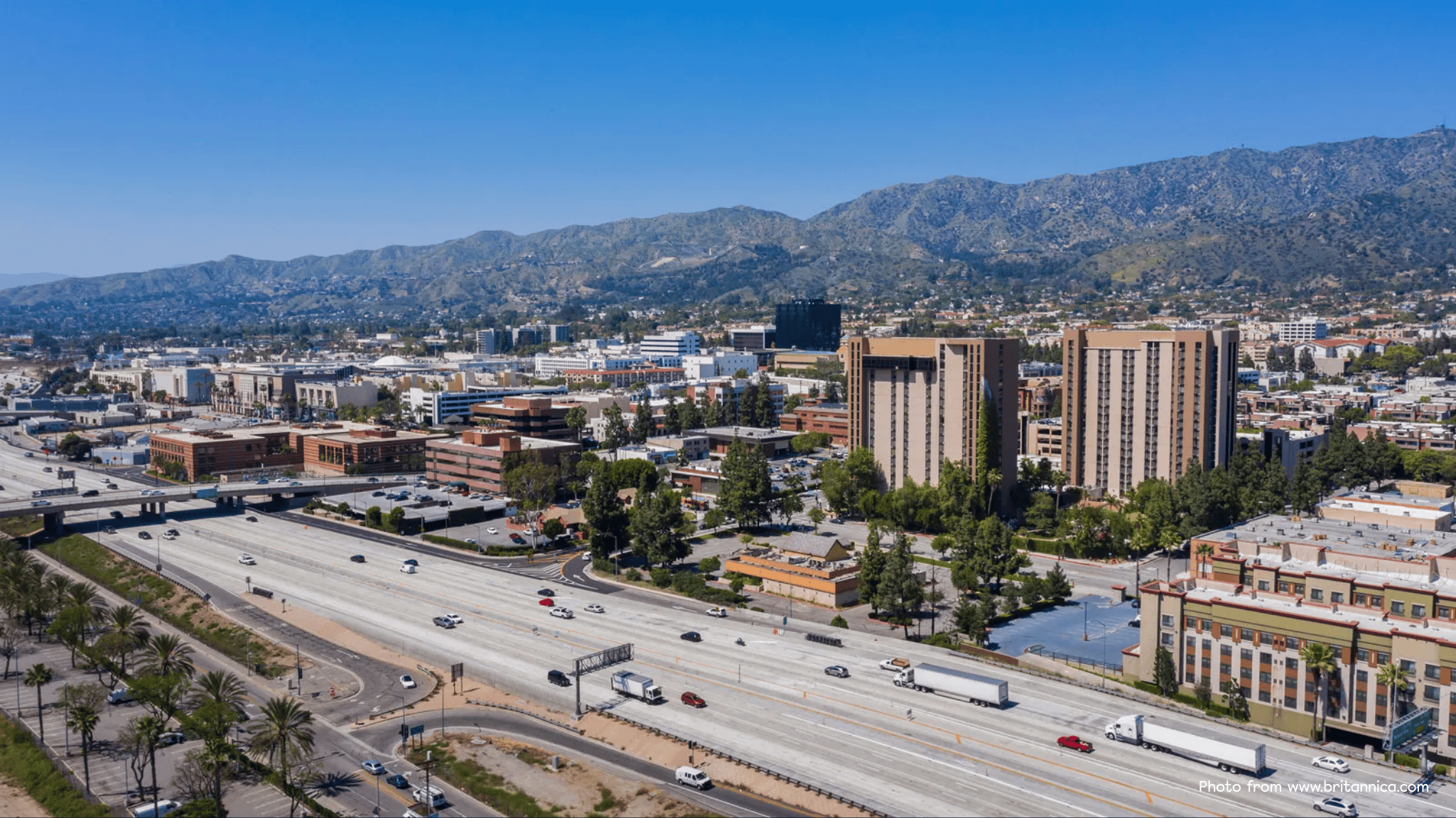 Aerial view of Burbank, California with office buildings, residential neighborhoods, and the 5 Freeway against the Verdugo Mountains on a clear day.