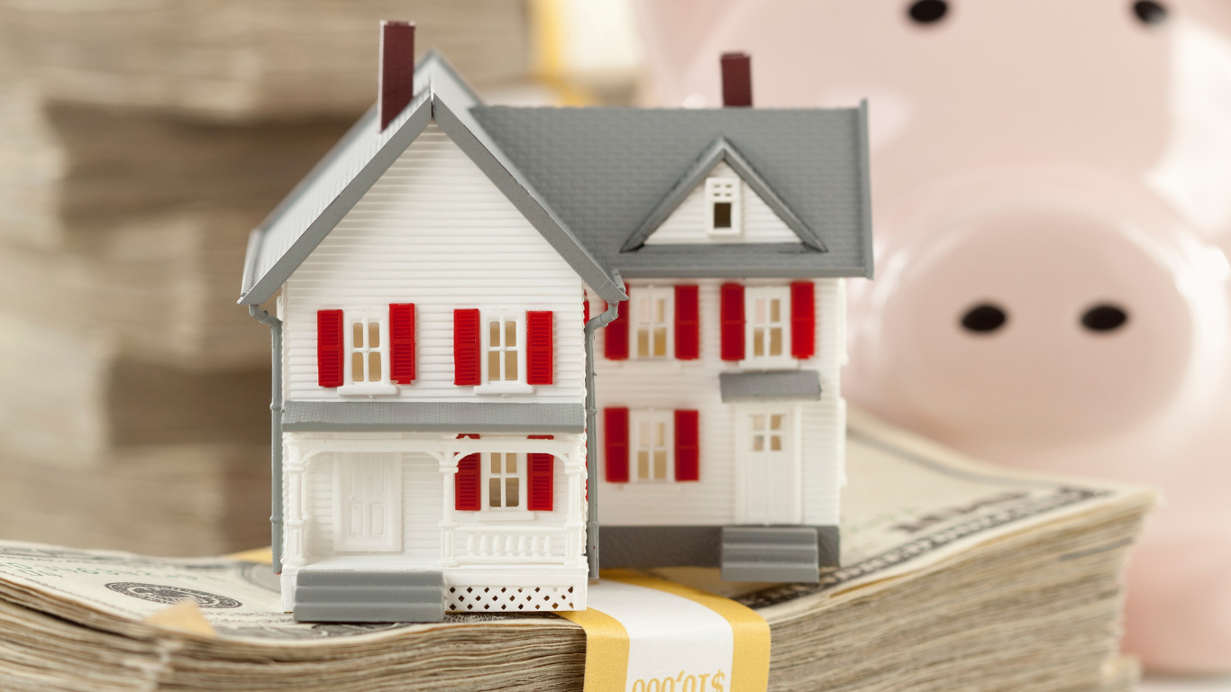 Miniature house model placed on stacks of dollar bills with a piggy bank in the background, representing using home equity lines of credit (HELOCs) and credit lines for financial security and real estate investment