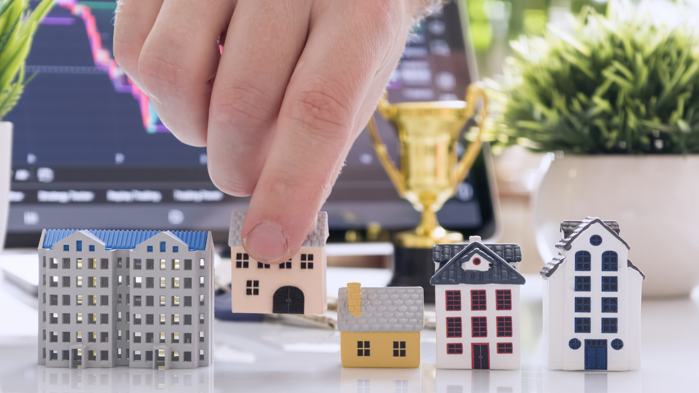 Person selecting between miniature model homes representing residential, multifamily, and commercial real estate investments, symbolizing property investment strategy and portfolio building in Los Angeles.
