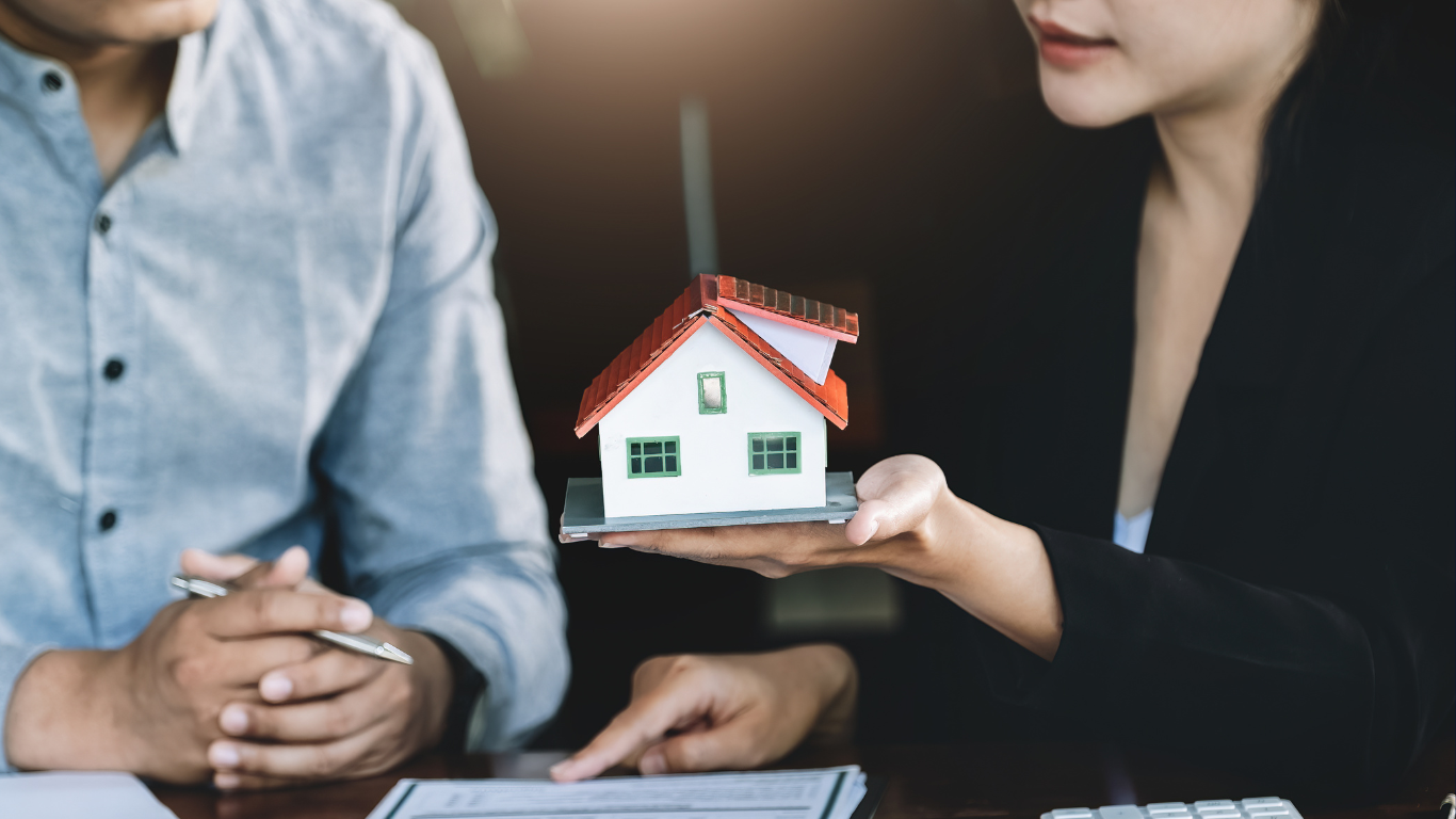 Real estate agent and client discussing home refinancing options while holding a miniature house model, symbolizing building equity and compounding wealth through smart property investments.