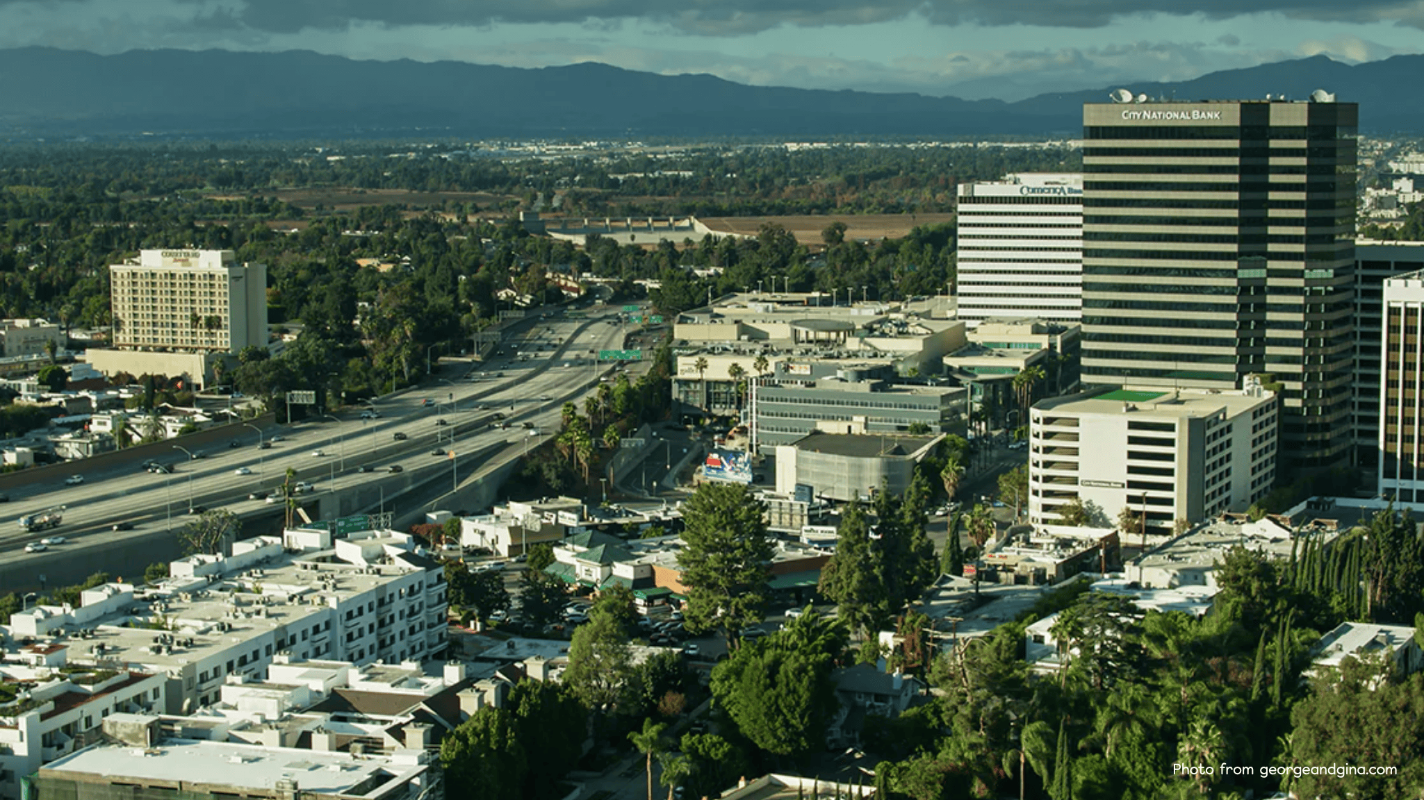 Aerial view of Sherman Oaks featuring the 101 Freeway, commercial high-rises, residential neighborhoods, and the San Fernando Valley landscape in the distance.