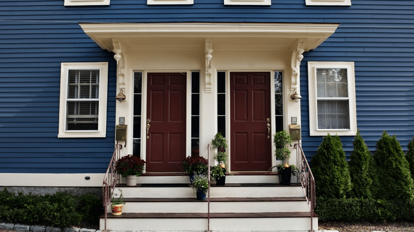 Front view of a blue duplex house with two red entry doors, white trim, and potted plants — example of a 2–4 unit property ideal for real estate investing and house hacking.