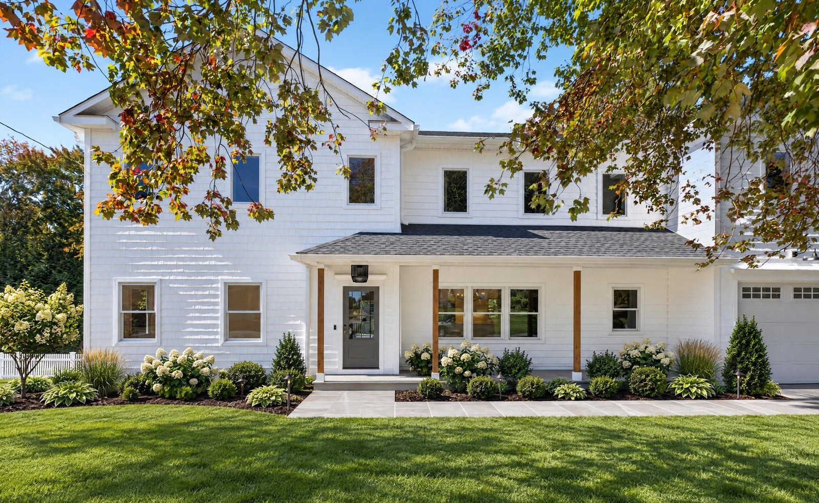White colonial with a covered front porch, landscaped beds and an attached garage