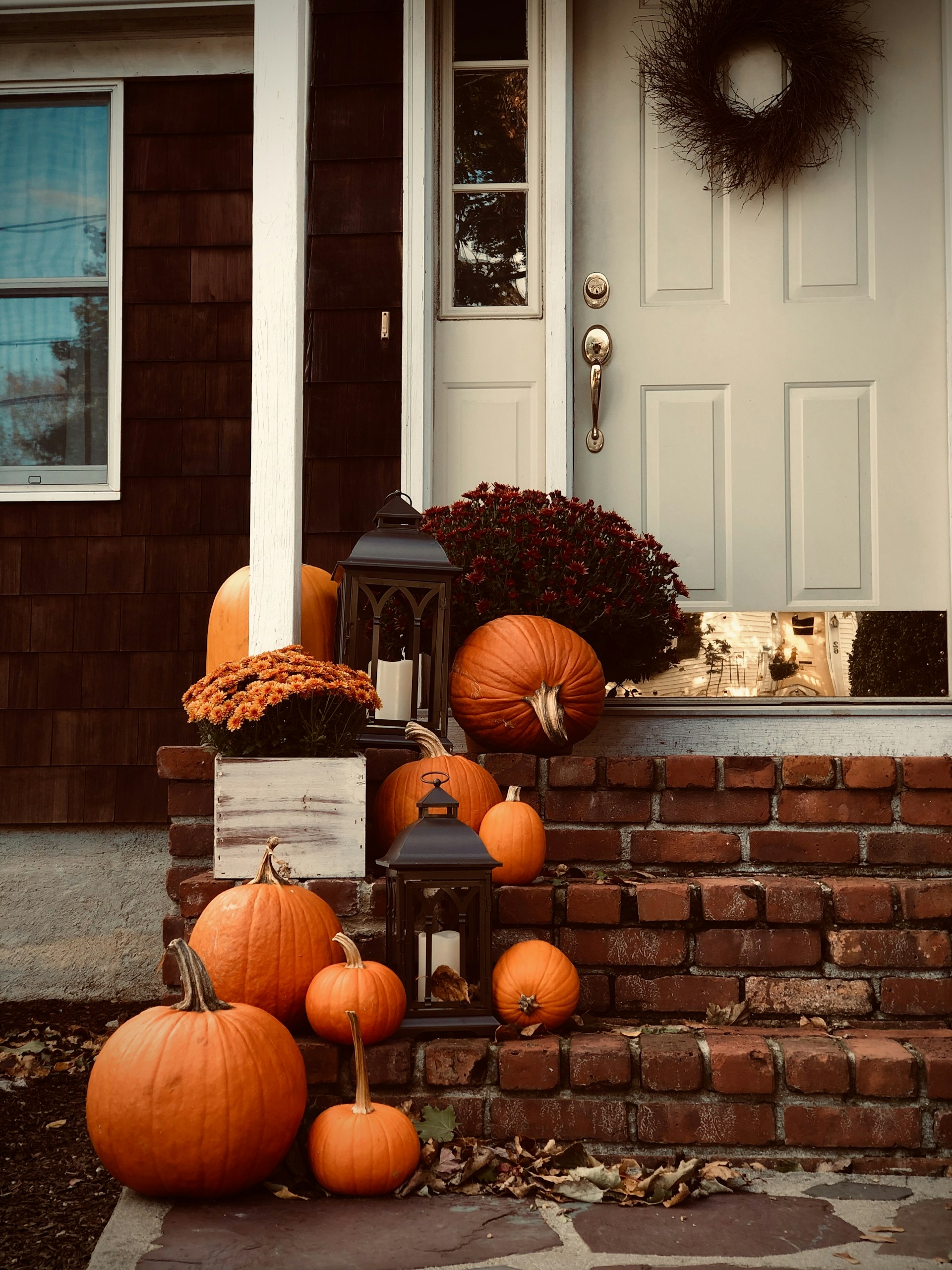Autumn front porch with pumpkins, mums and a lantern on brick steps