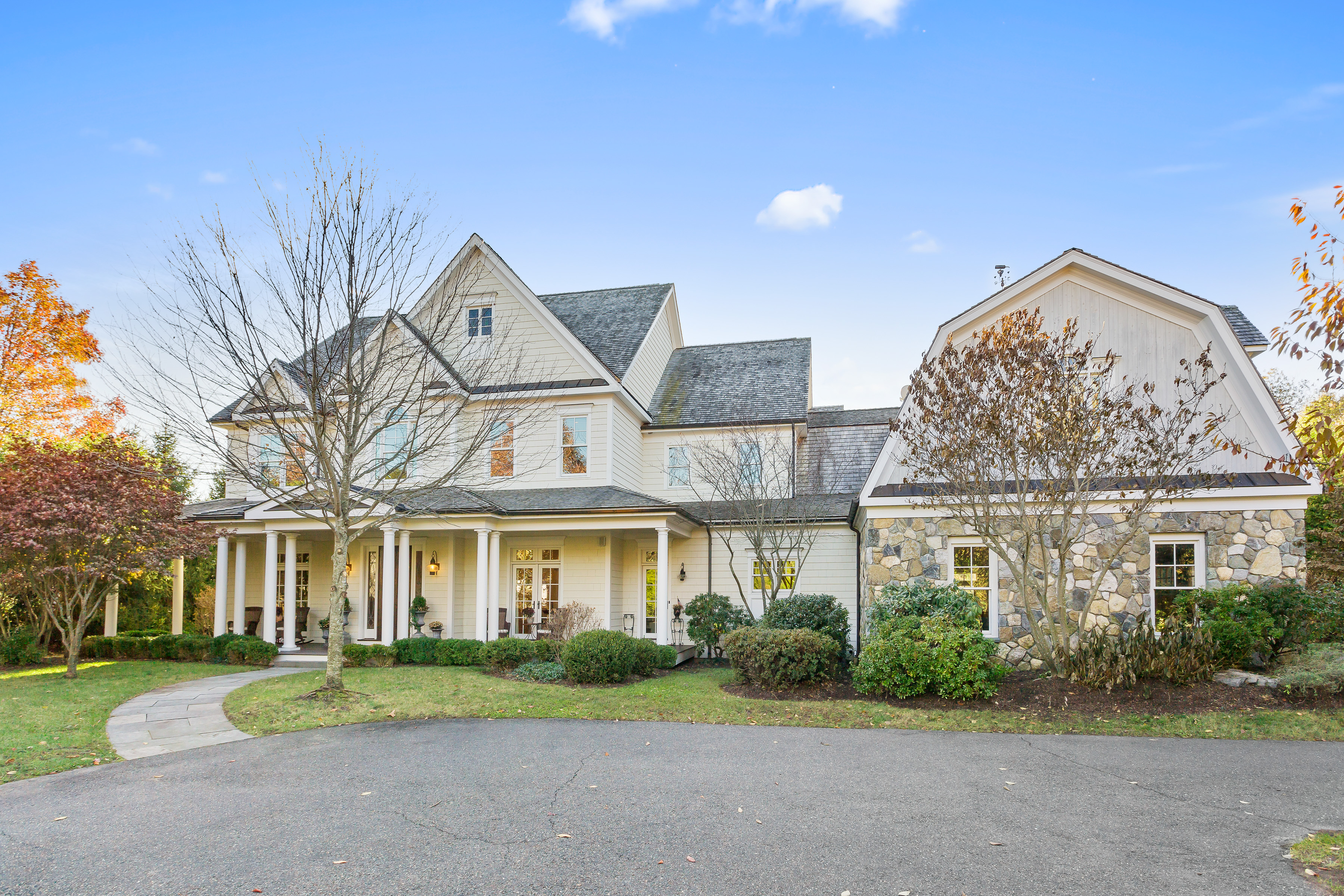 A shingled Connecticut colonial with a covered porch and landscaped front yard on a fall afternoon