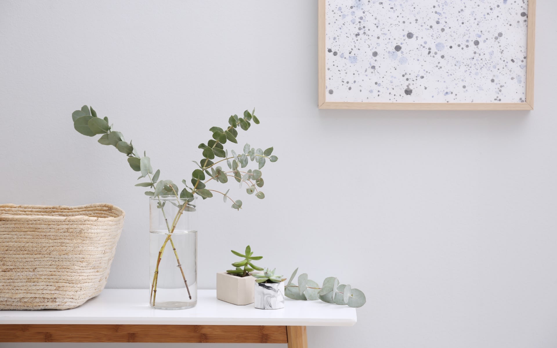 Console table with eucalyptus in a vase, woven basket and framed art