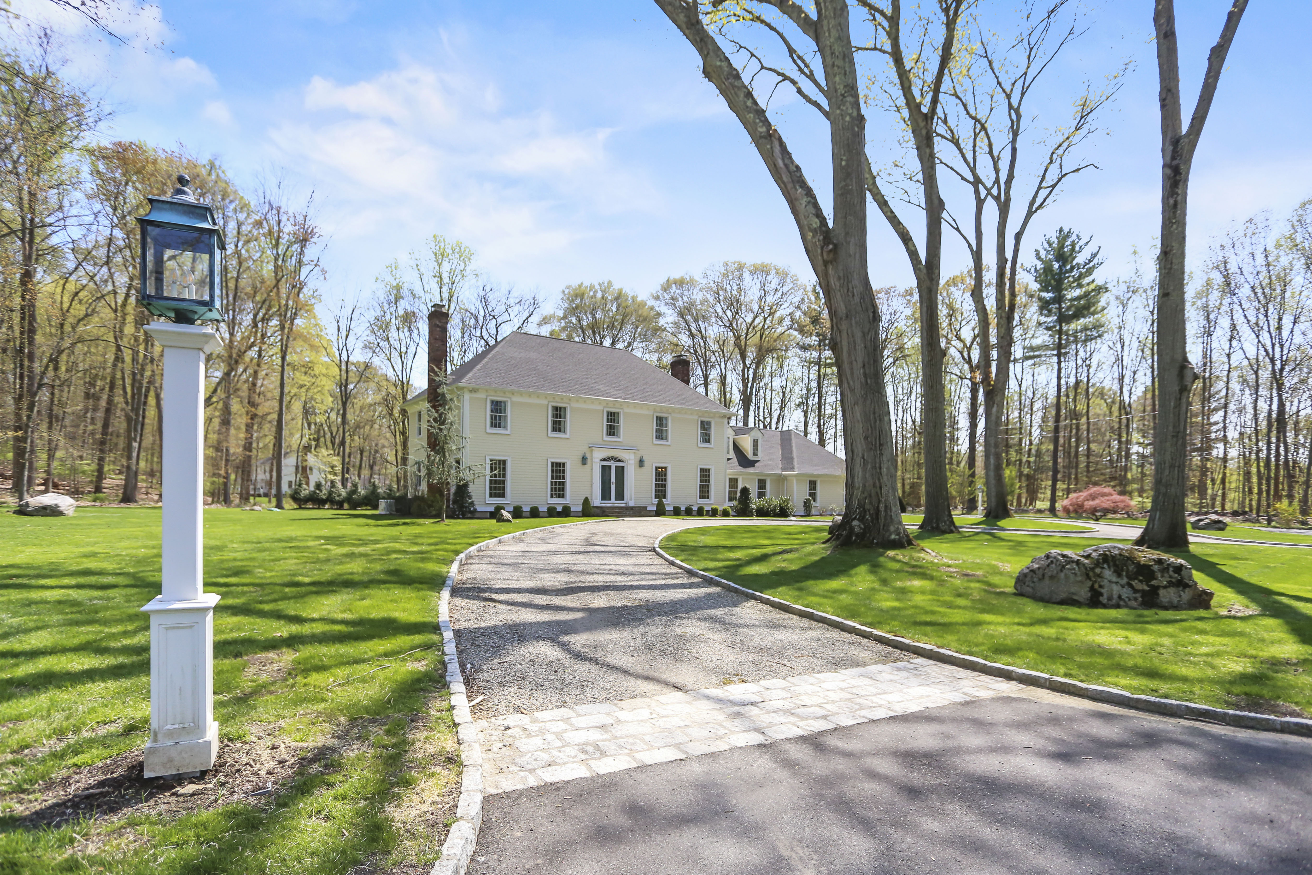 White colonial set back on a wooded lot with a long driveway and lamppost in Fairfield County CT