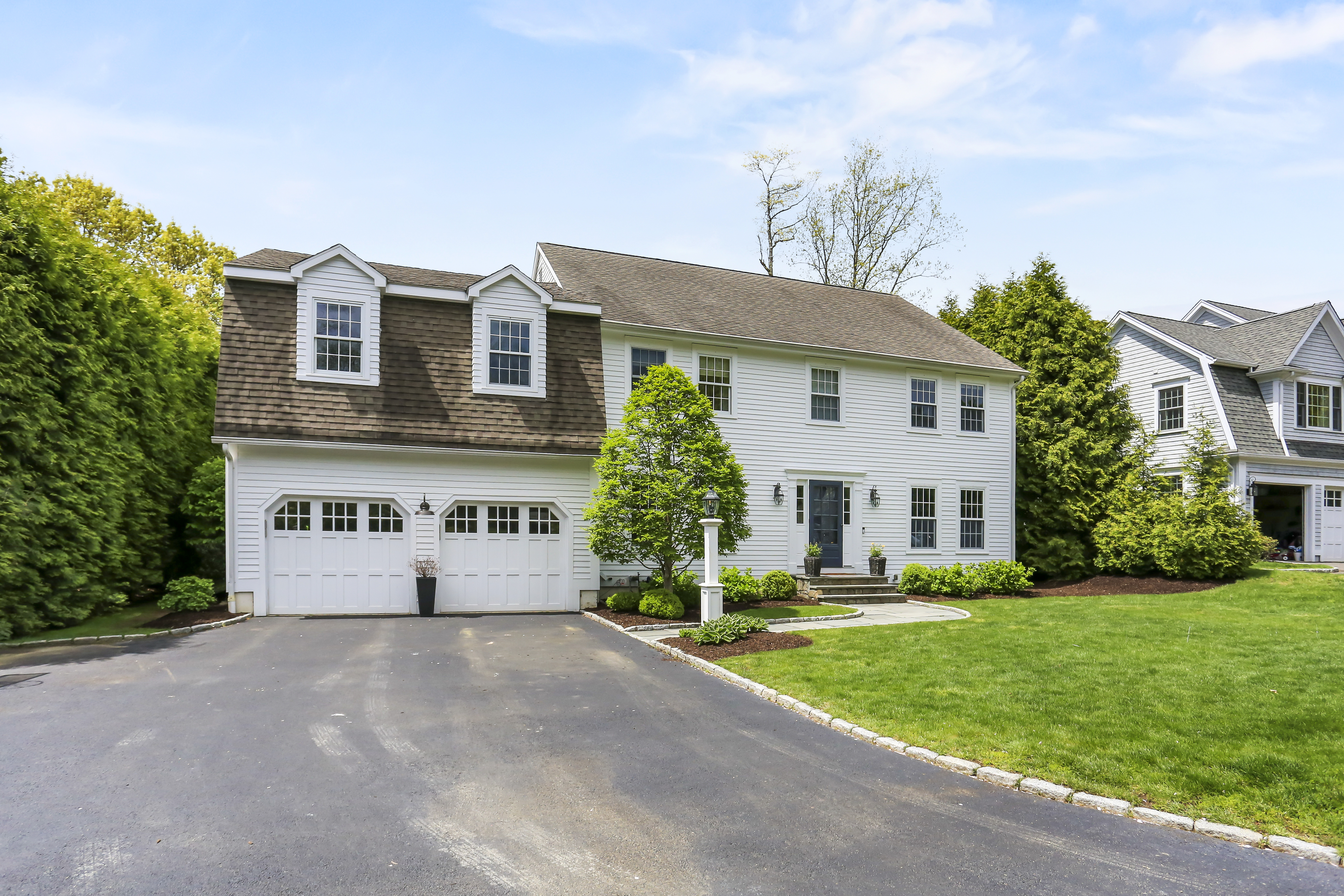 Colonial home with an attached garage, wide driveway and green lawn on a sunny summer day in Fairfield County CT