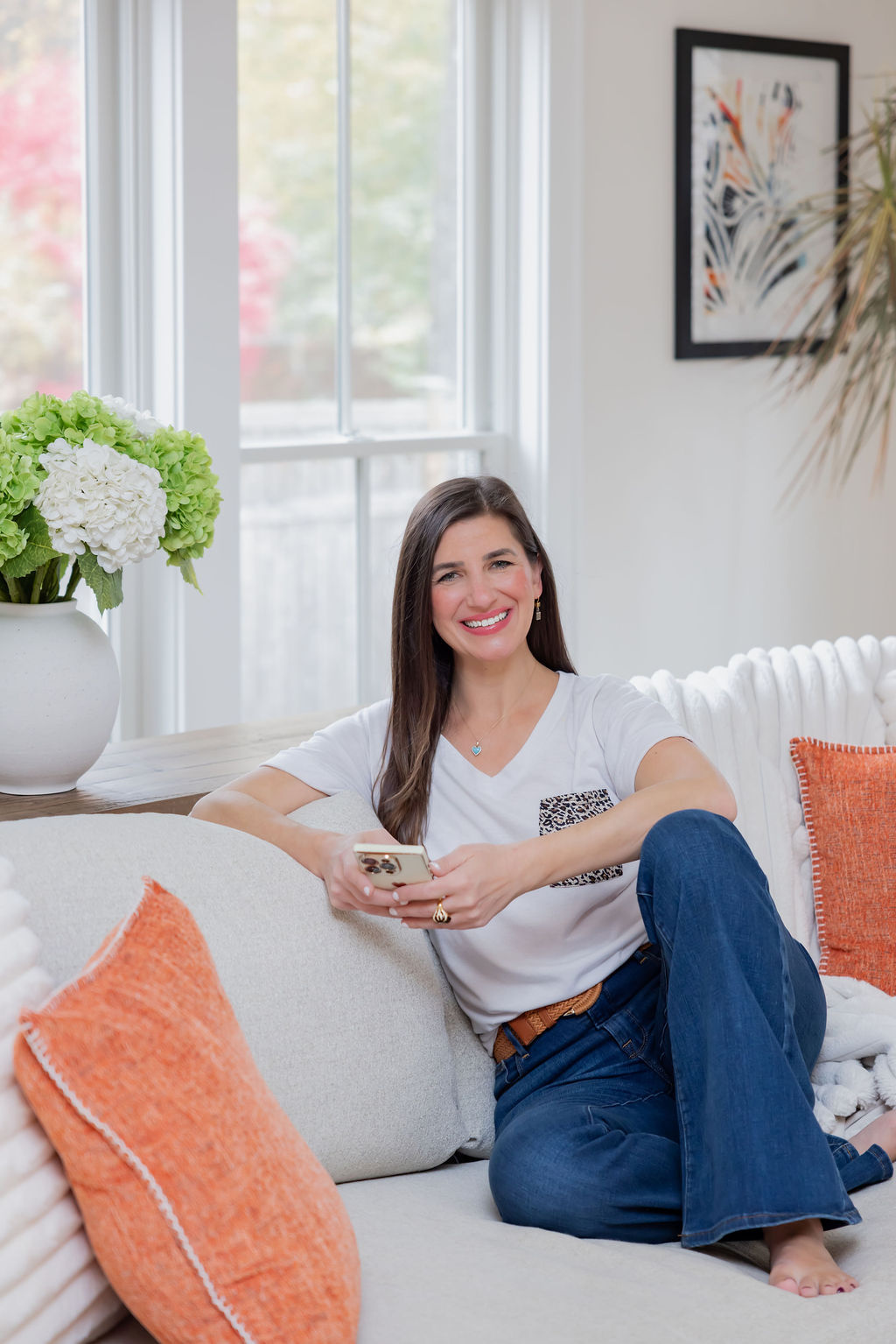 Shoshana Snyder, Realtor with Compass Connecticut, smiling on a sofa with her phone in hand.