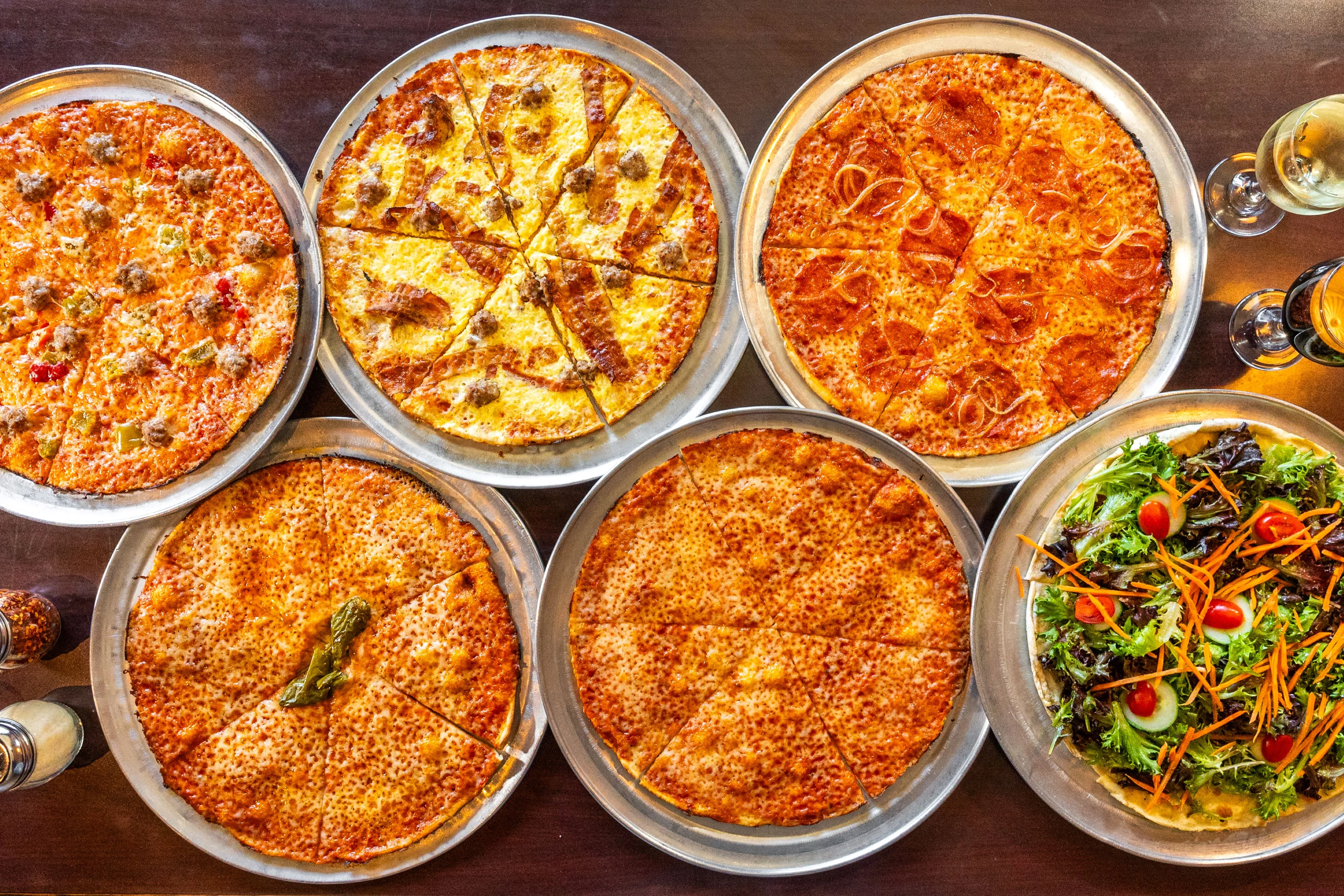 Overhead view of several pizzas and a salad spread across a wooden table