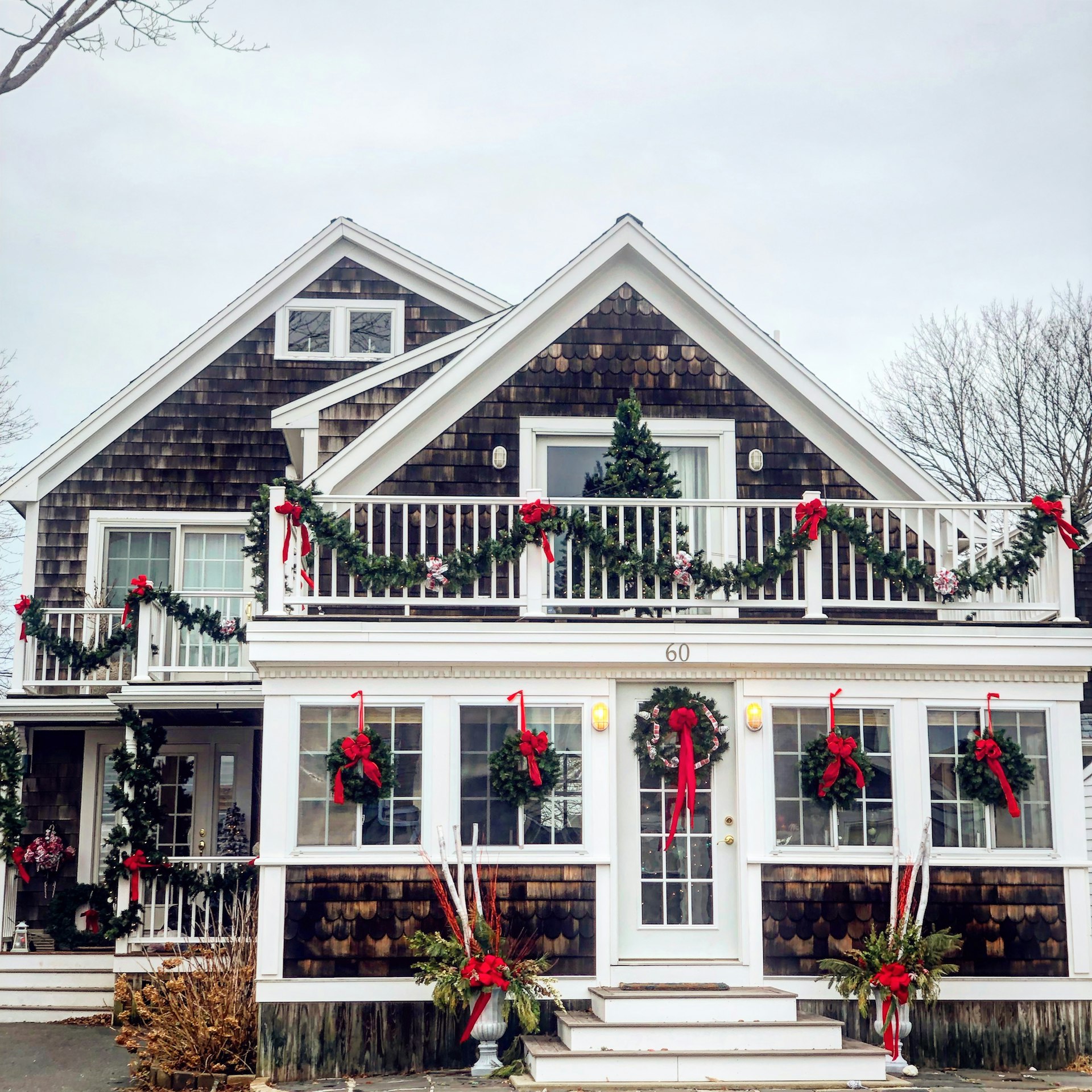 Shingled coastal home decorated with holiday wreaths and red bows in the snow