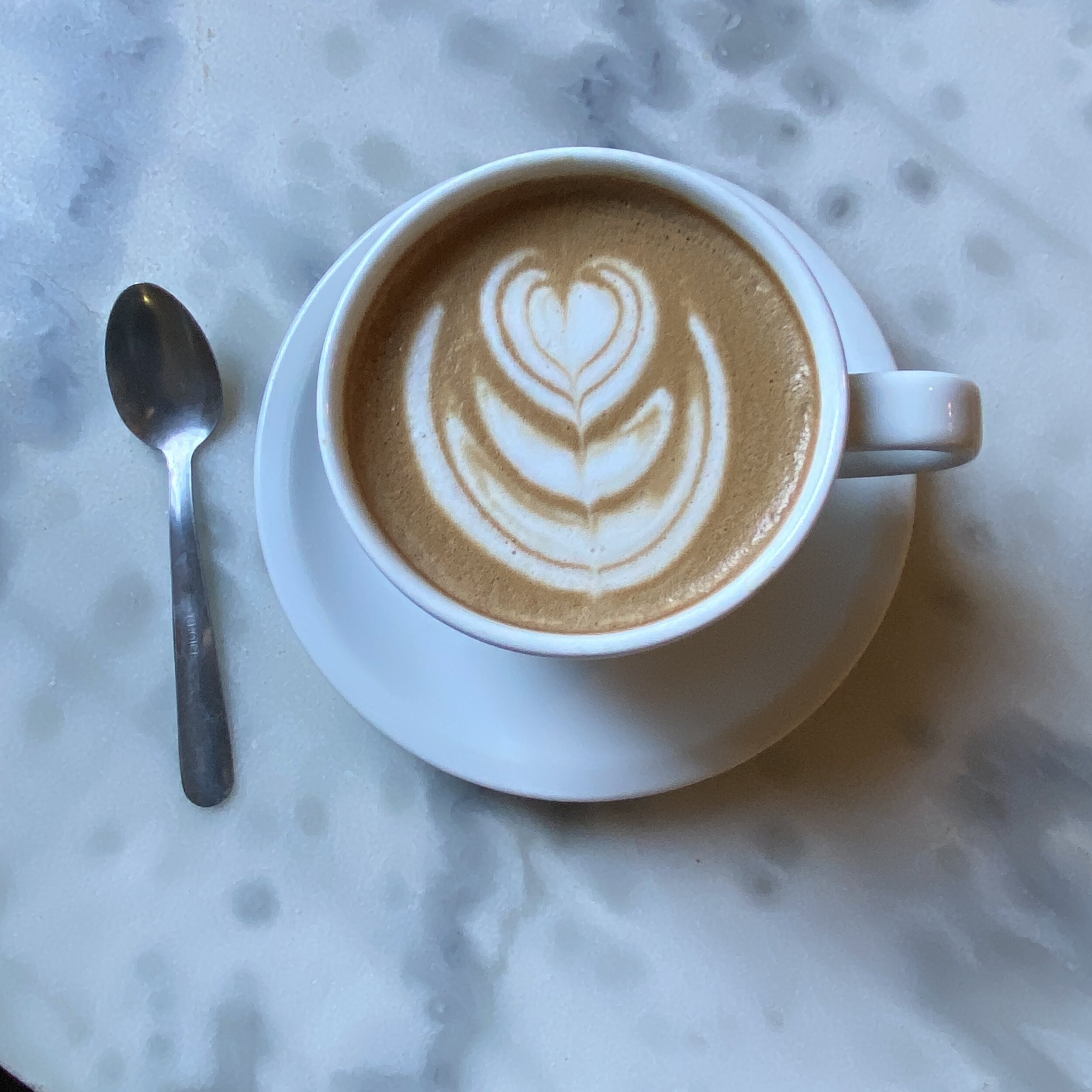 Latte with heart-shaped foam art in a white cup and saucer on a marble table