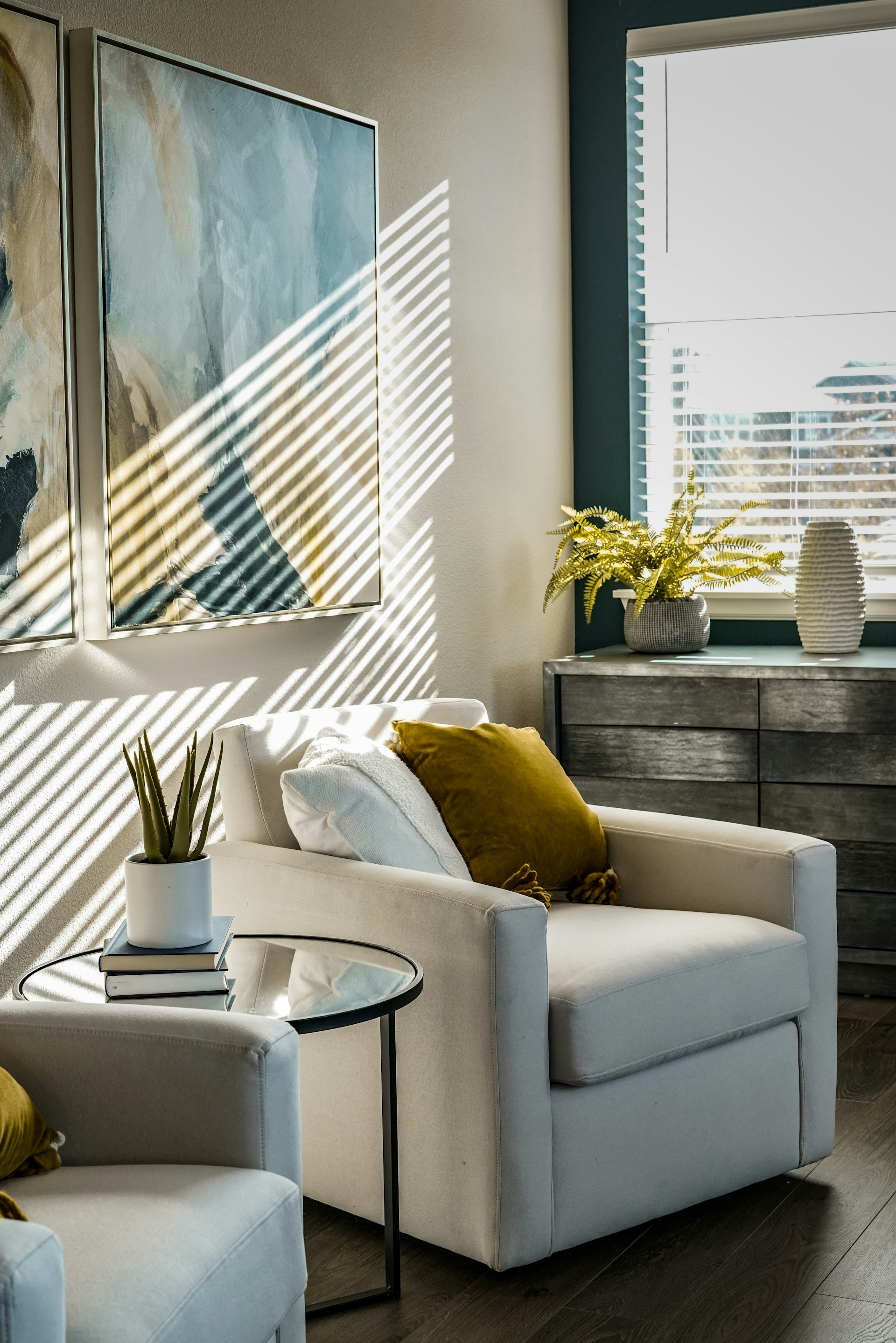 Sunlit living room corner with mustard pillow, plants and a wood dresser