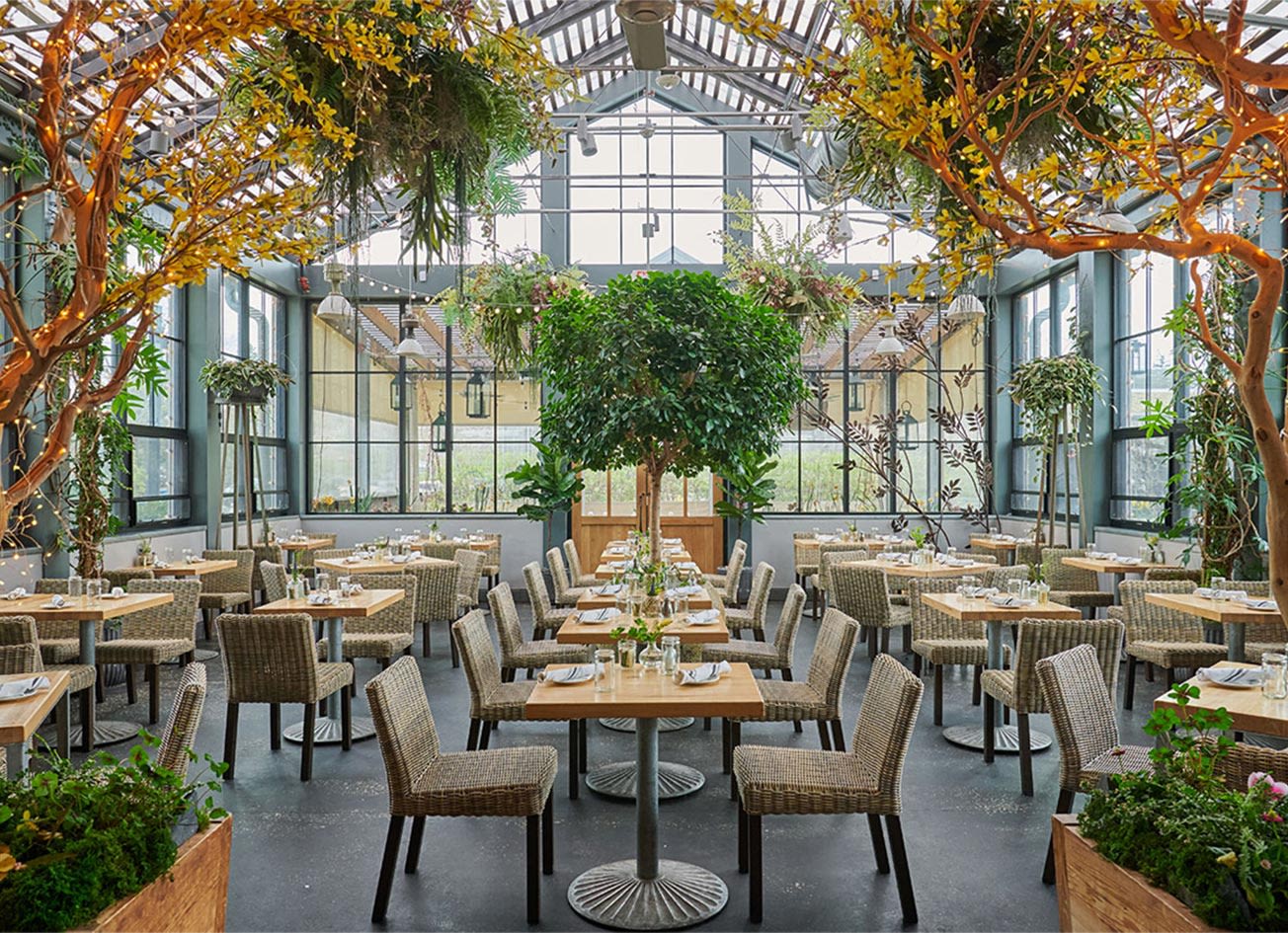 Glass-enclosed garden dining room with climbing greenery, string lights and set tables at a Fairfield County restaurant