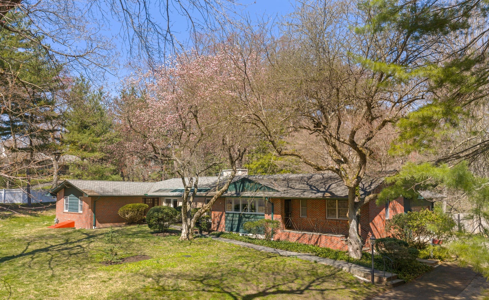 Long brick mid-century modern ranch set back behind a lawn, mature trees and a flowering tree in bloom