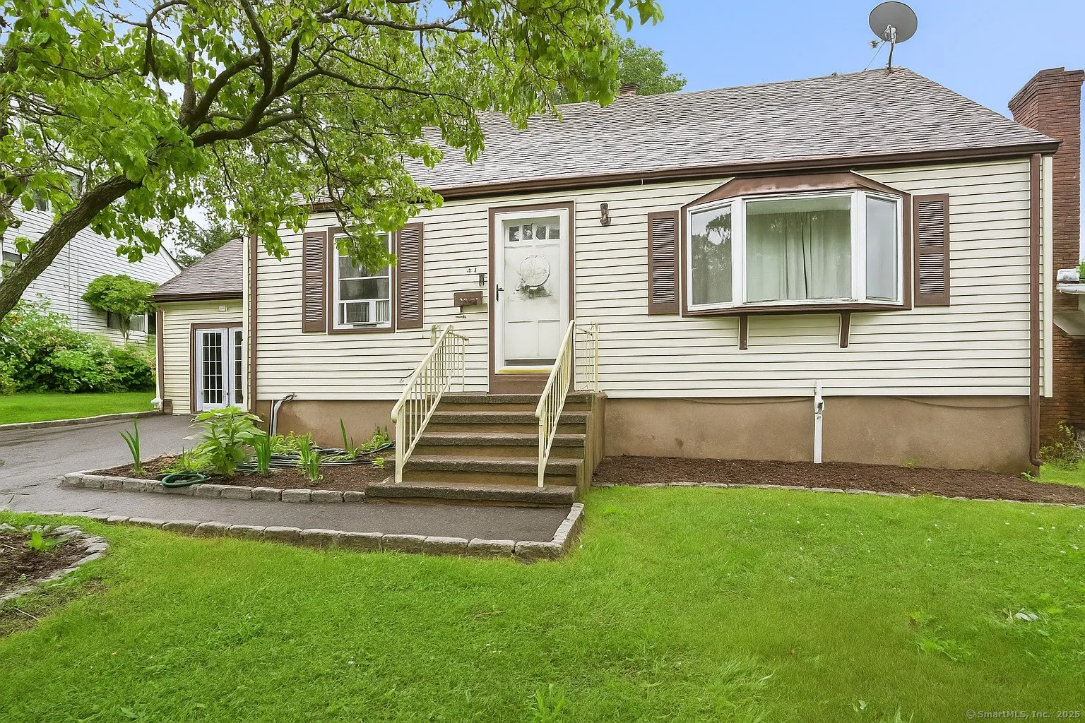 Cream-colored cape with a bay window and front steps on a landscaped lot at 84 Hickory Street, West Haven CT