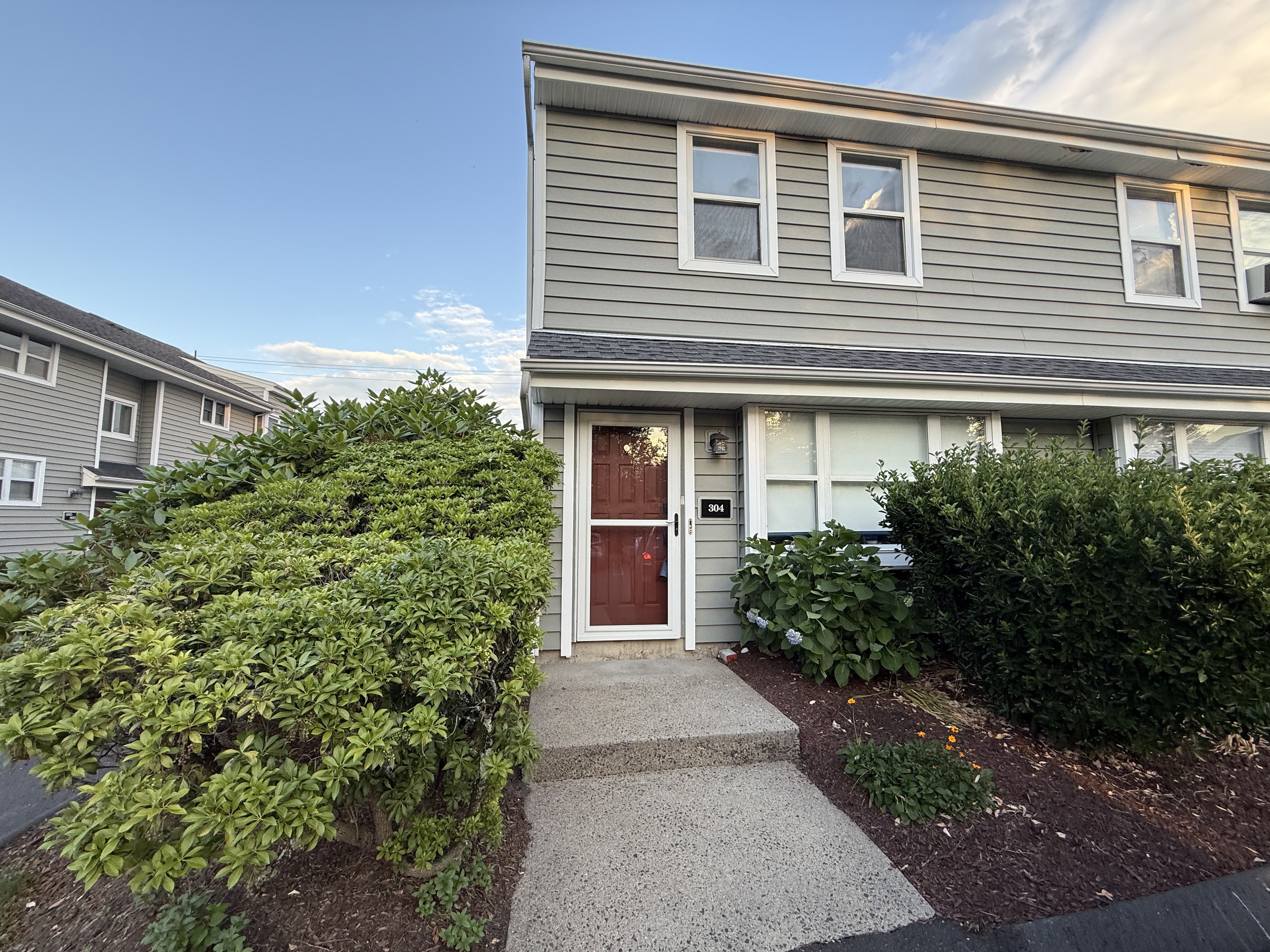 End-unit townhouse with a red front door and mature shrubs in the Silver Sands community, Milford CT