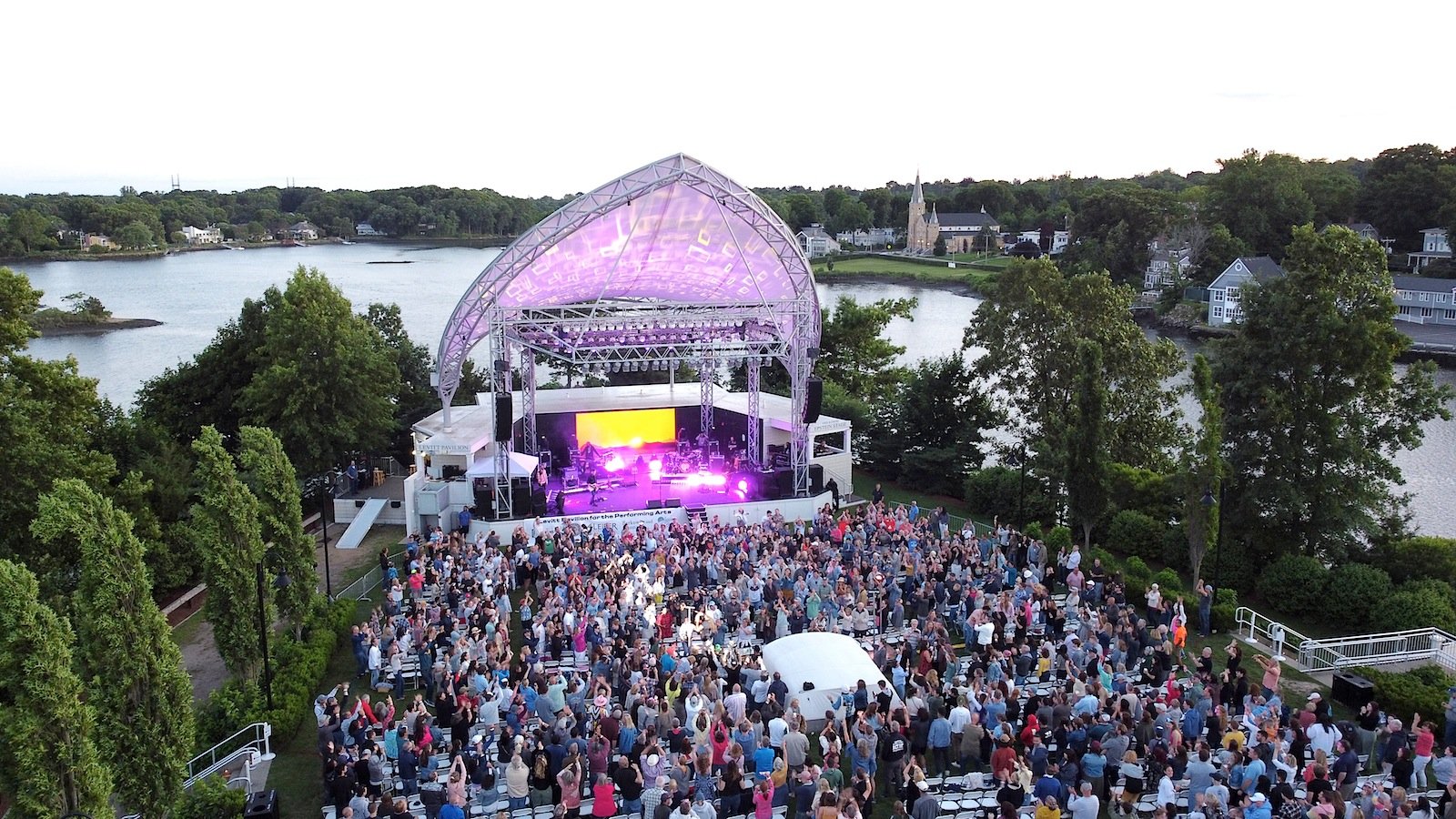 Crowd gathered on the lawn at an outdoor evening concert beside the water in Westport CT