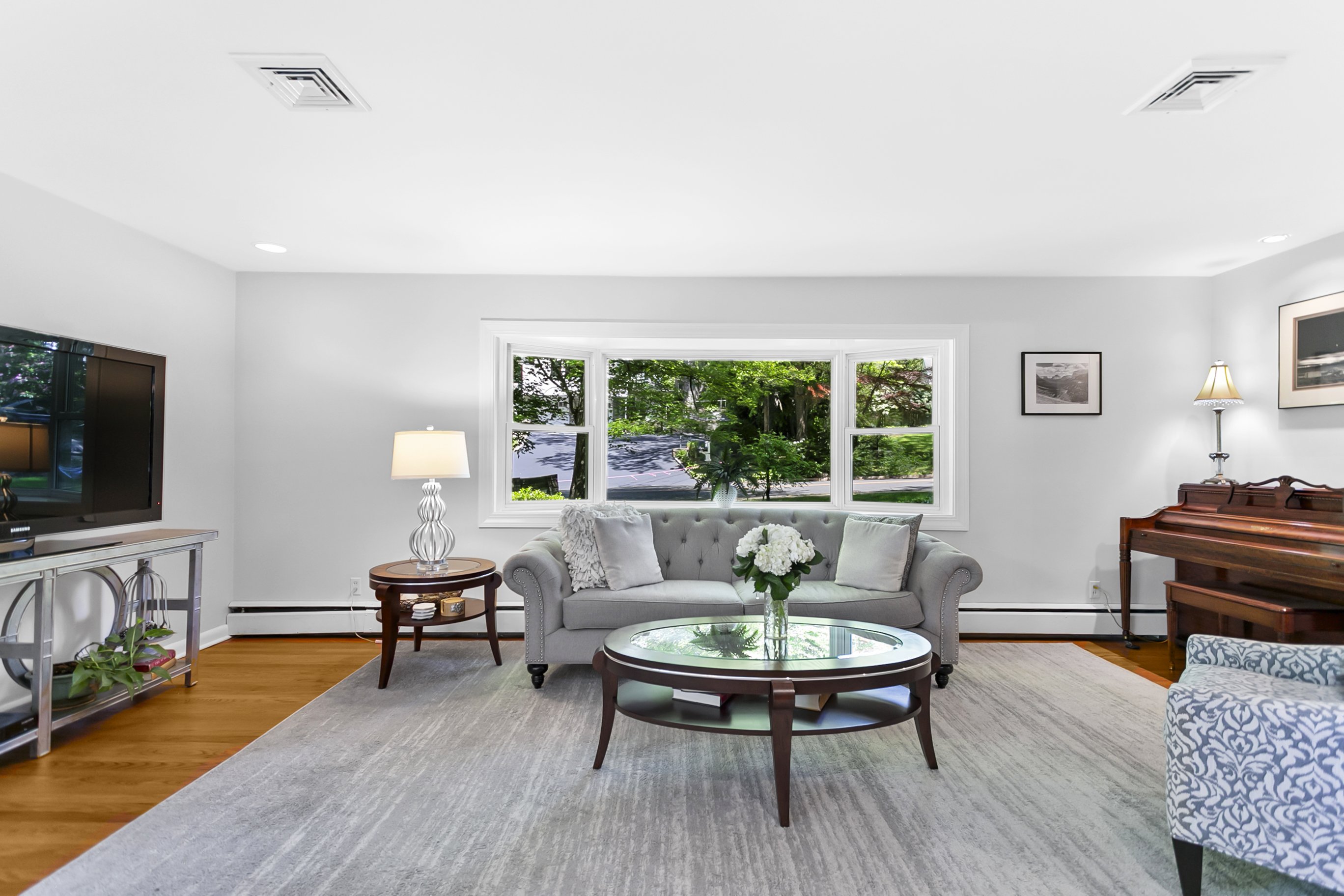 Bright living room with a gray sofa, coffee table and windows looking onto greenery at 219 Jackman Avenue, Fairfield CT