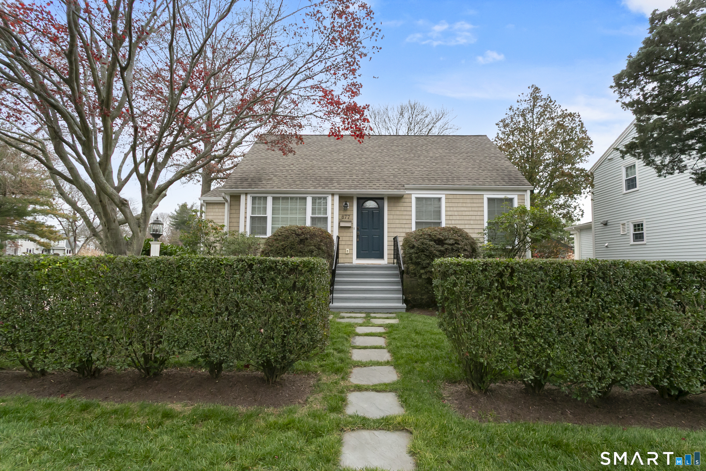 Cape-style home behind manicured hedges with a flowering tree in Fairfield Beach