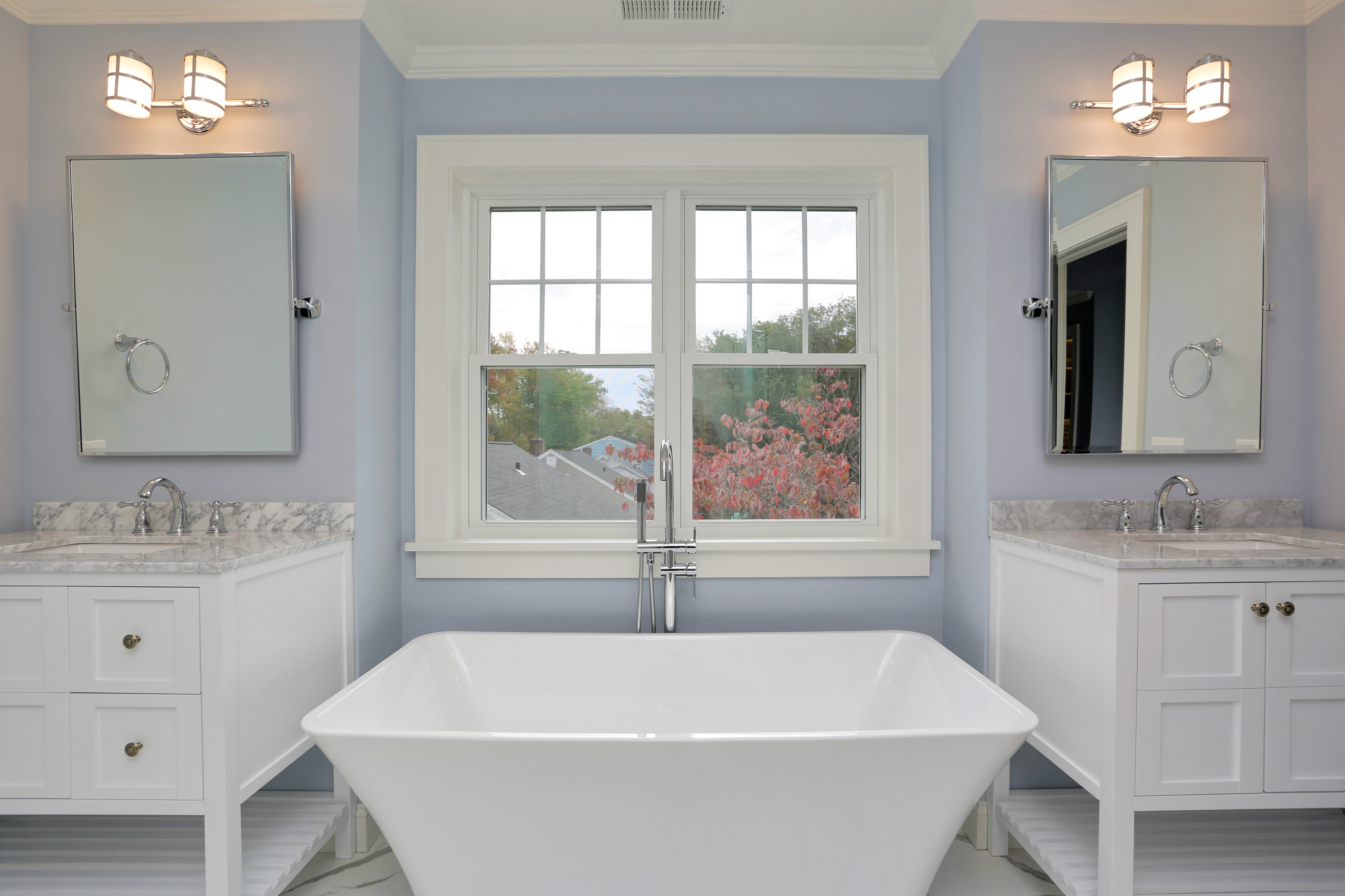Bright primary bathroom with a freestanding tub, double vanities and a garden window