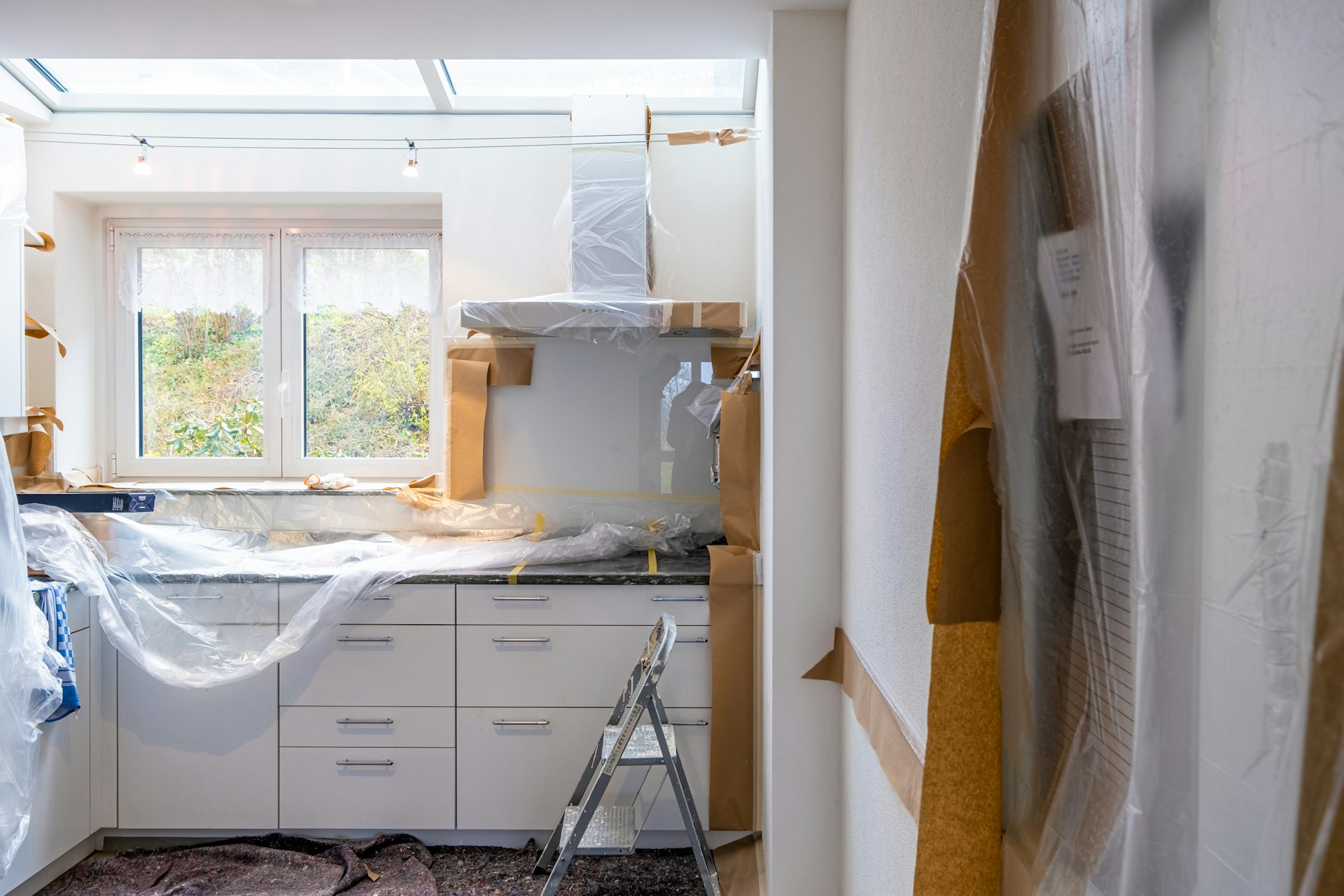 Kitchen mid-renovation with drop cloths, ladder and plastic sheeting