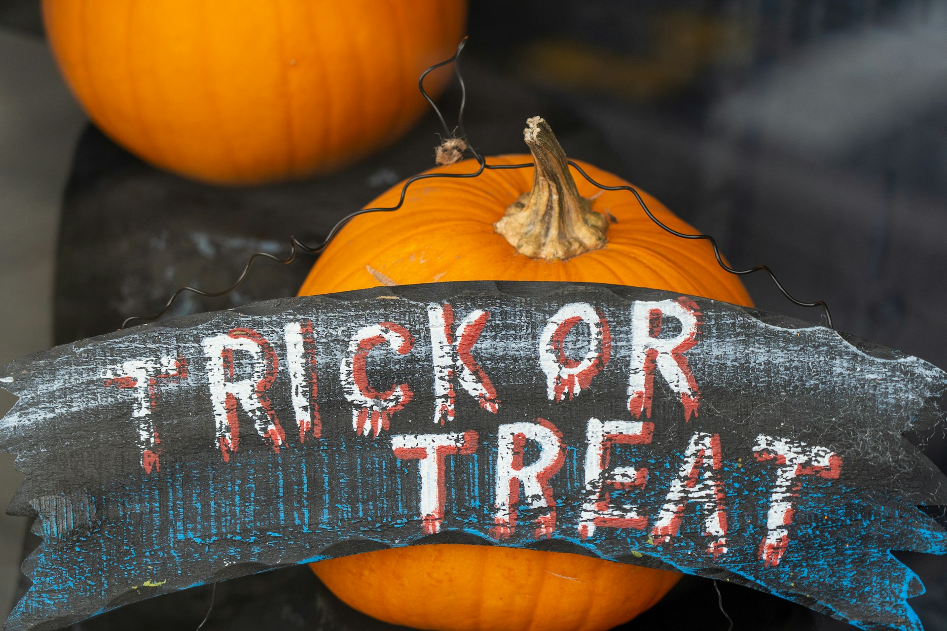 Hand-painted “Trick or Treat” sign propped against pumpkins on a porch