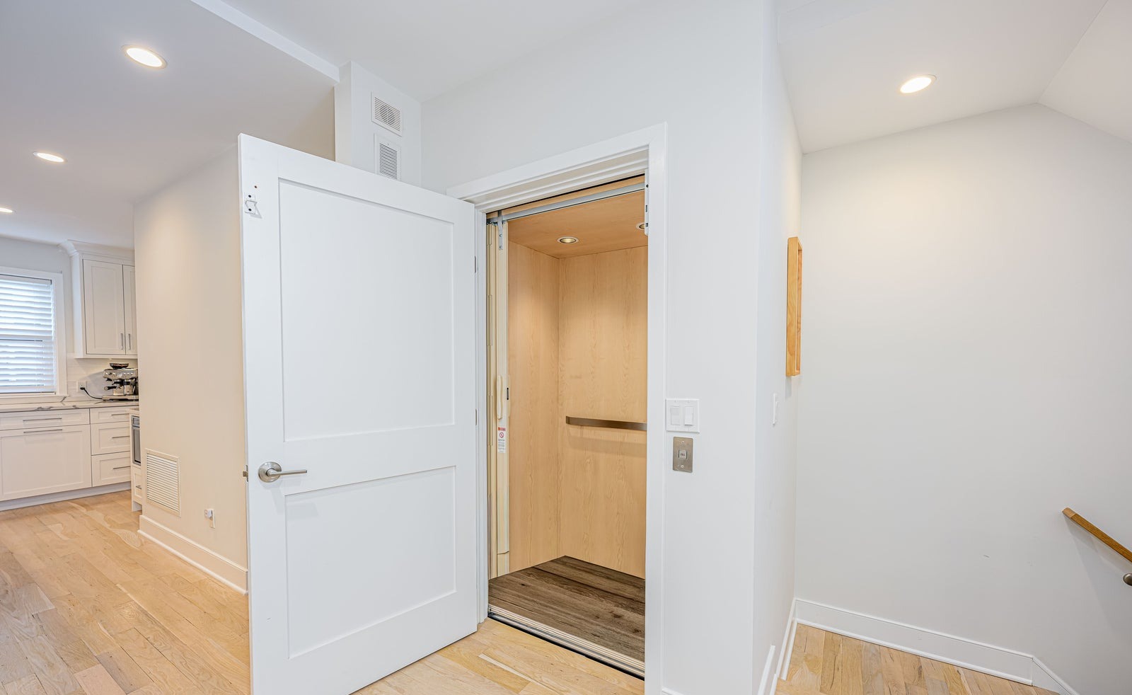 Private residential elevator with a wood-panelled interior opening onto a hardwood hallway