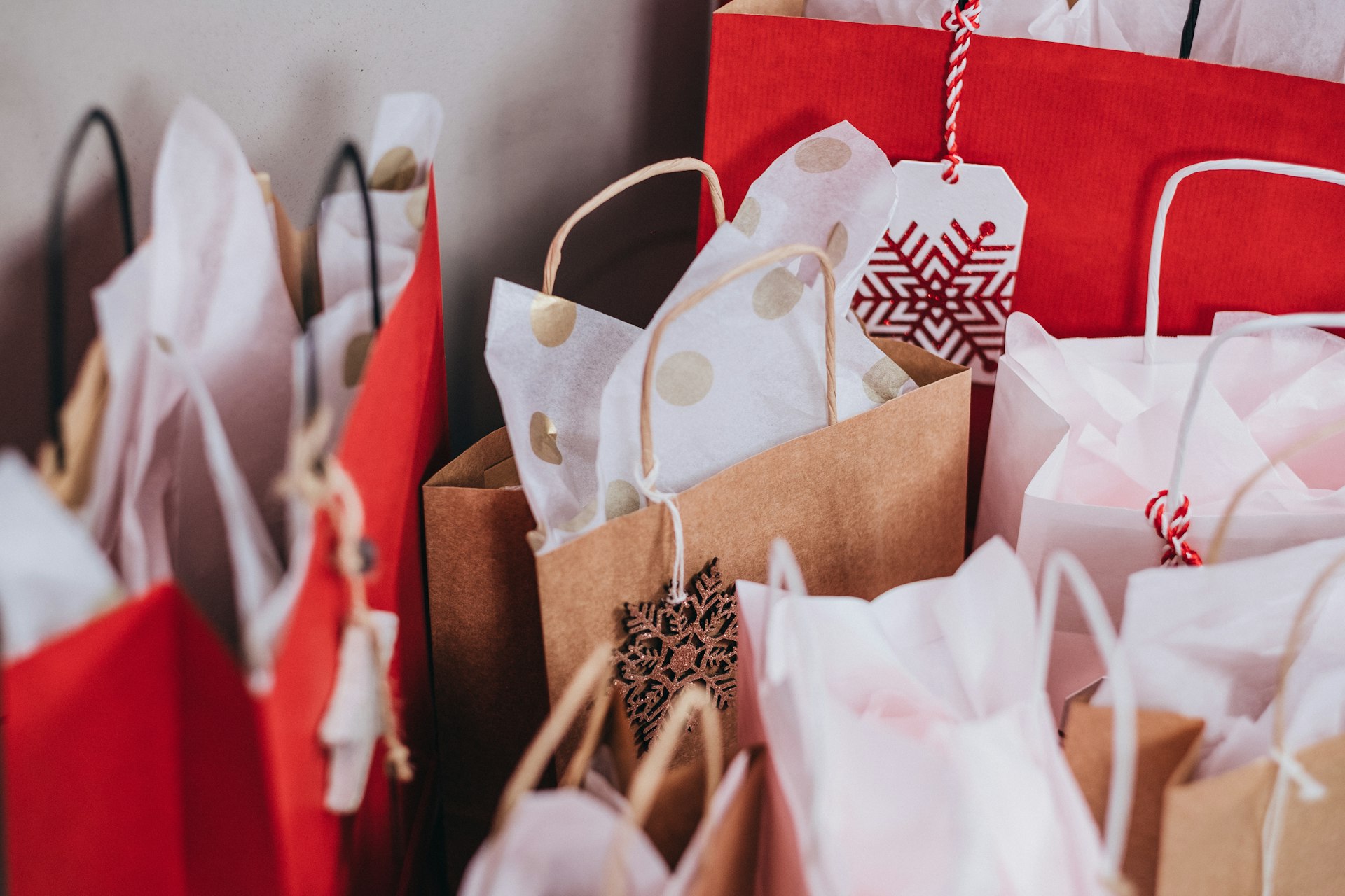 Holiday shopping bags with ribbon and ornament tags lined up on a bench