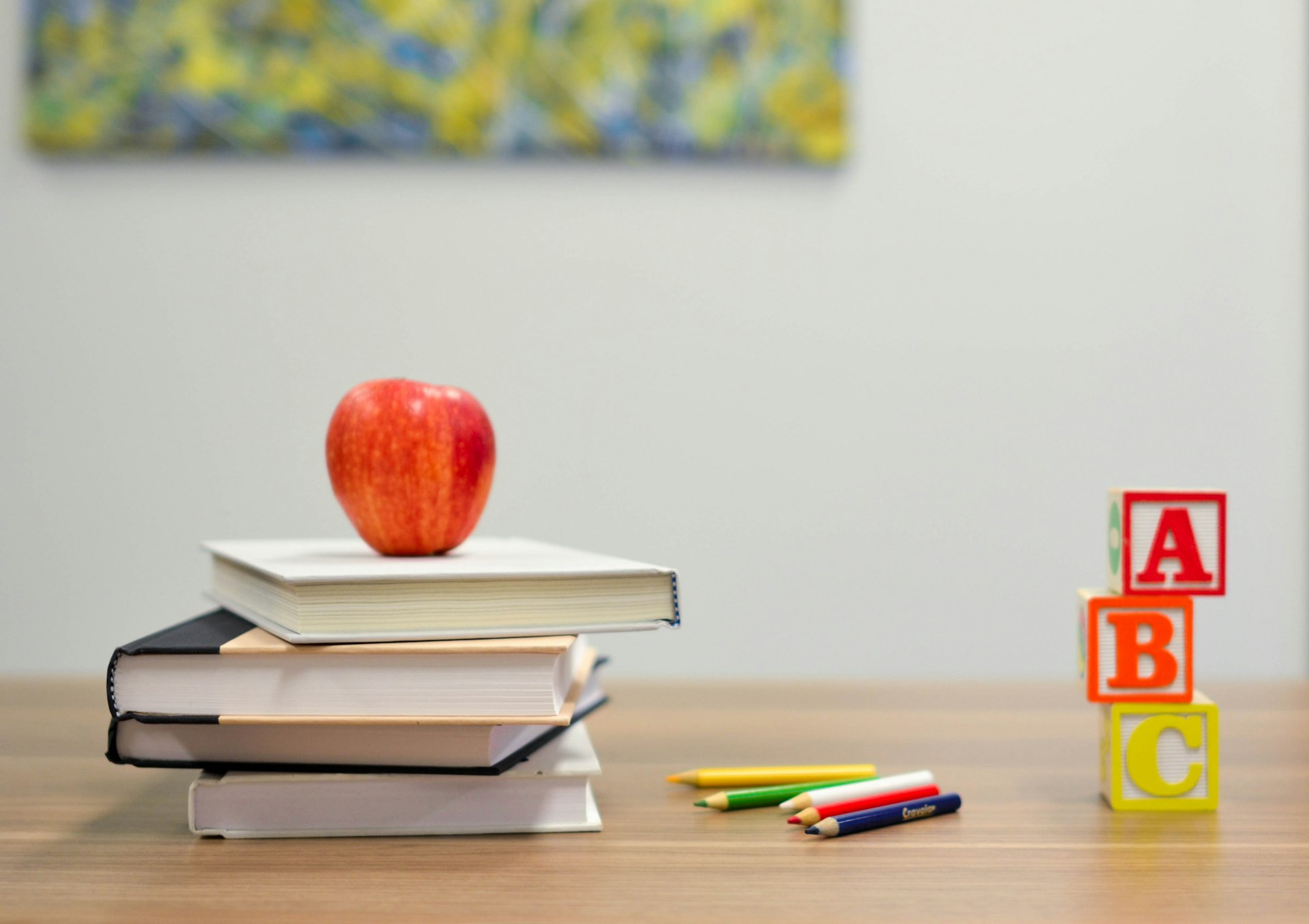 Red apple on a stack of books beside ABC blocks and colored pencils