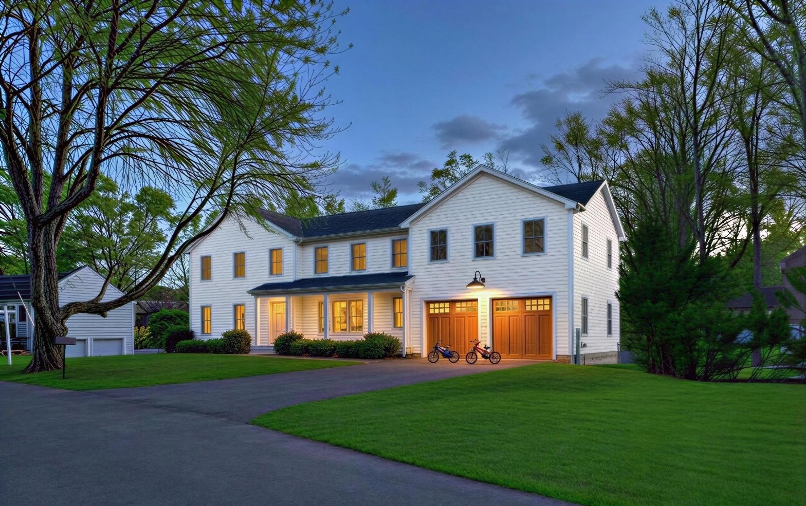 Front elevation of a white two-story colonial with a covered porch and attached two-car garage at dusk