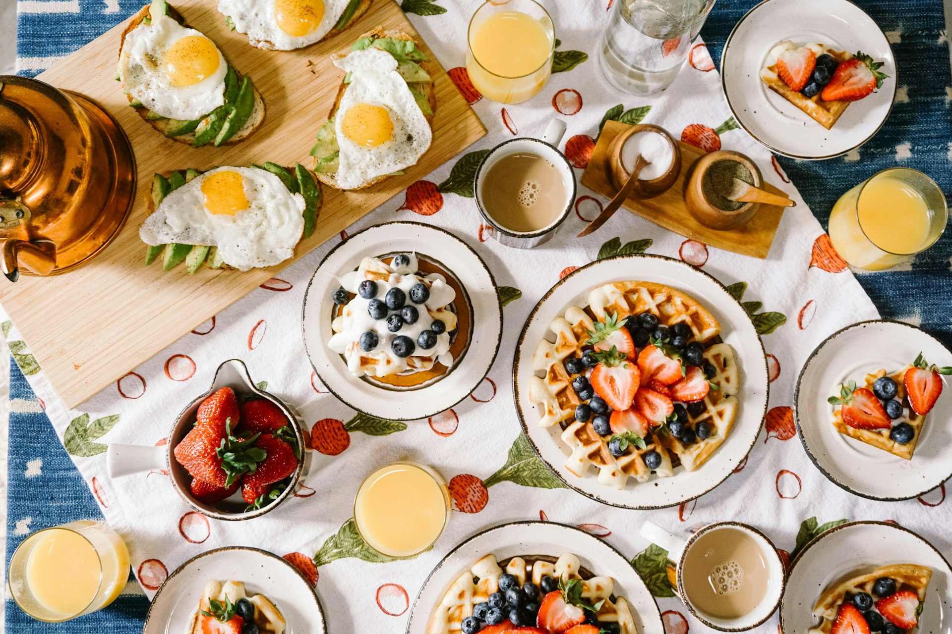 Overhead view of a brunch spread with waffles, berries, eggs and mimosas