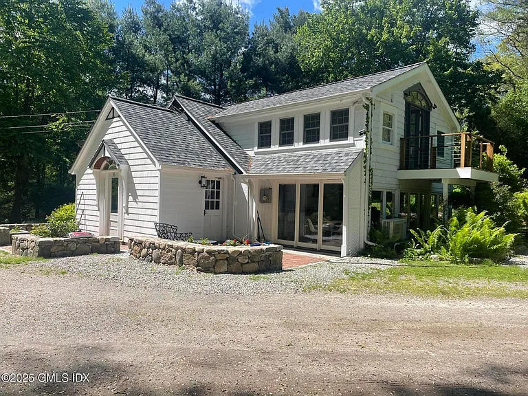 White cottage with a steep gabled roof and stone retaining wall on a wooded lot at 206 Sharp Hill Road, Wilton CT