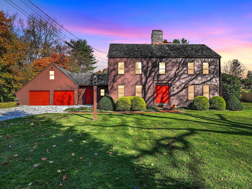 Saltbox colonial with red barn-style garage doors and lawn at dusk in Stratford, CT