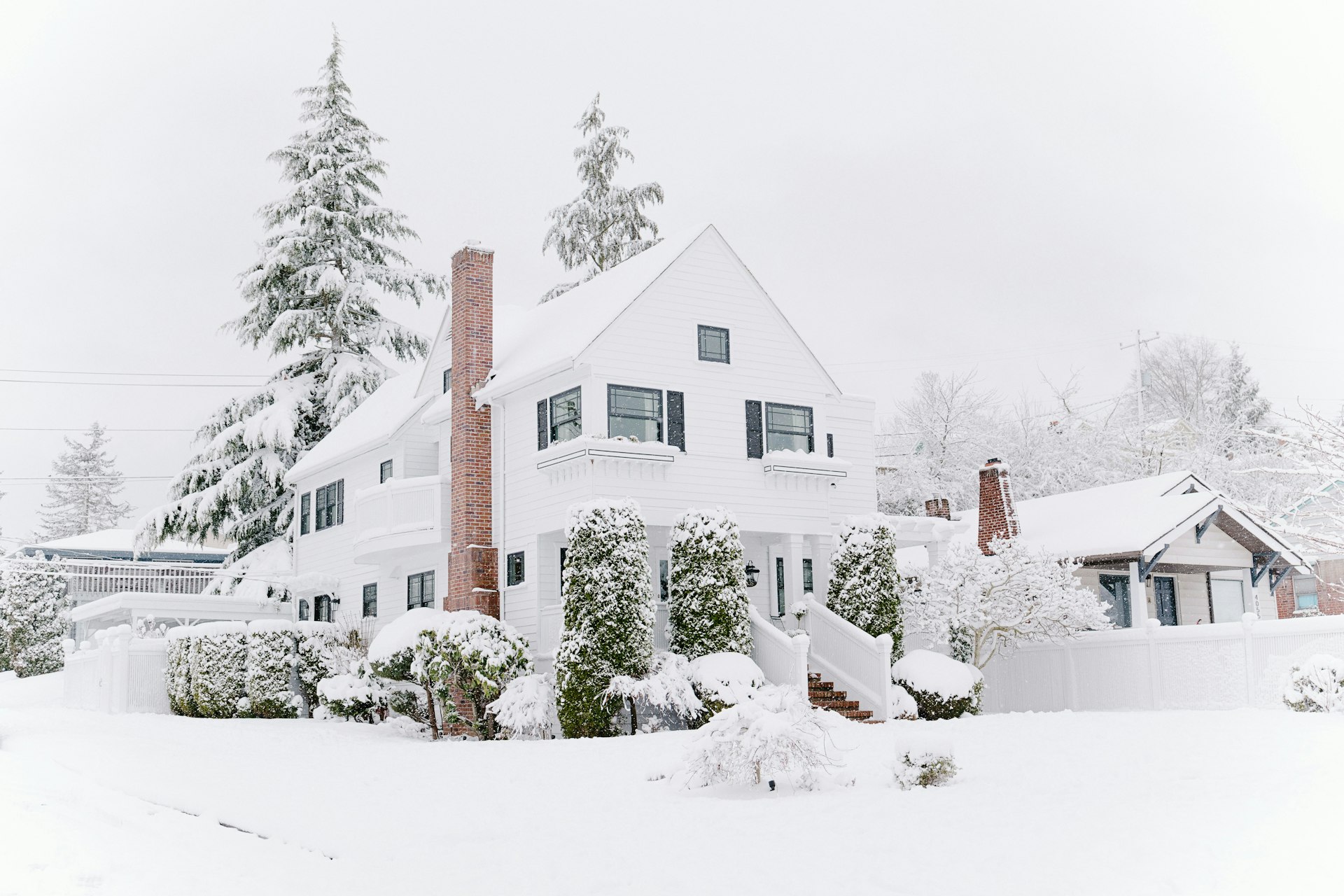 White colonial home surrounded by evergreens after a heavy snowfall