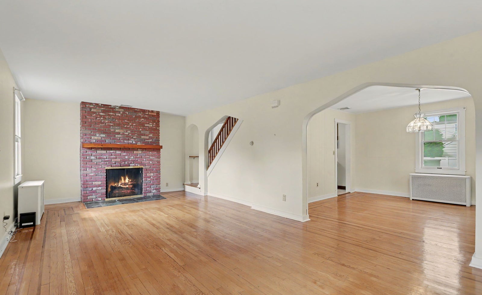 Living room with a brick fireplace, hardwood floors and an arched opening to the dining room