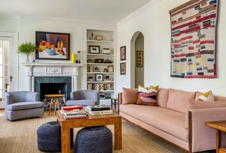 beige woven area rug pale pink sofa to right beneath textural artwork on white wall wood cocktail table with two pale...