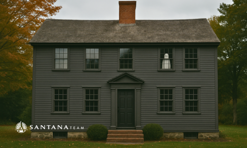 Historic New England house with subtle ghost in the upstairs window during autumn, representing the housing market’s spooky season theme.
