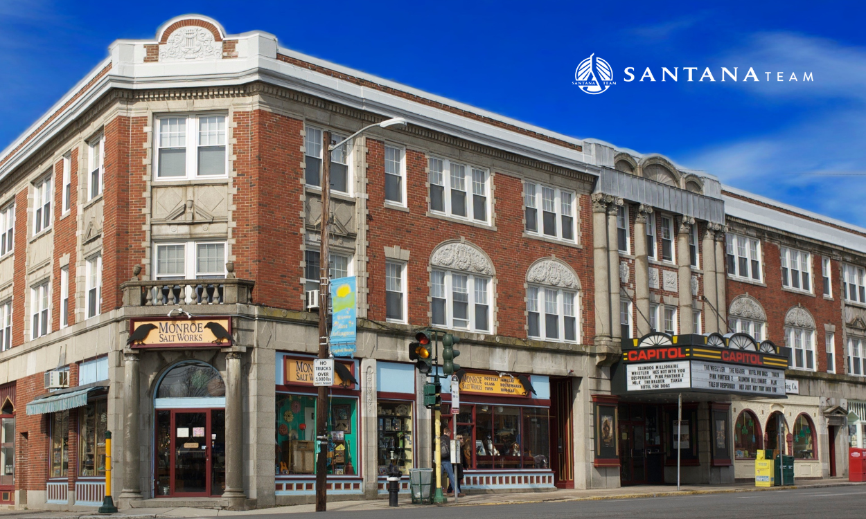View of Capitol Square in East Arlington featuring the historic Capitol Theatre and surrounding shops on Massachusetts Avenue, with blue sky overhead.