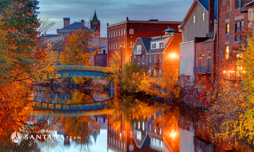 Mystic River in Medford MA at dusk with fall foliage, brick mill buildings, and green bridge reflecting on the water