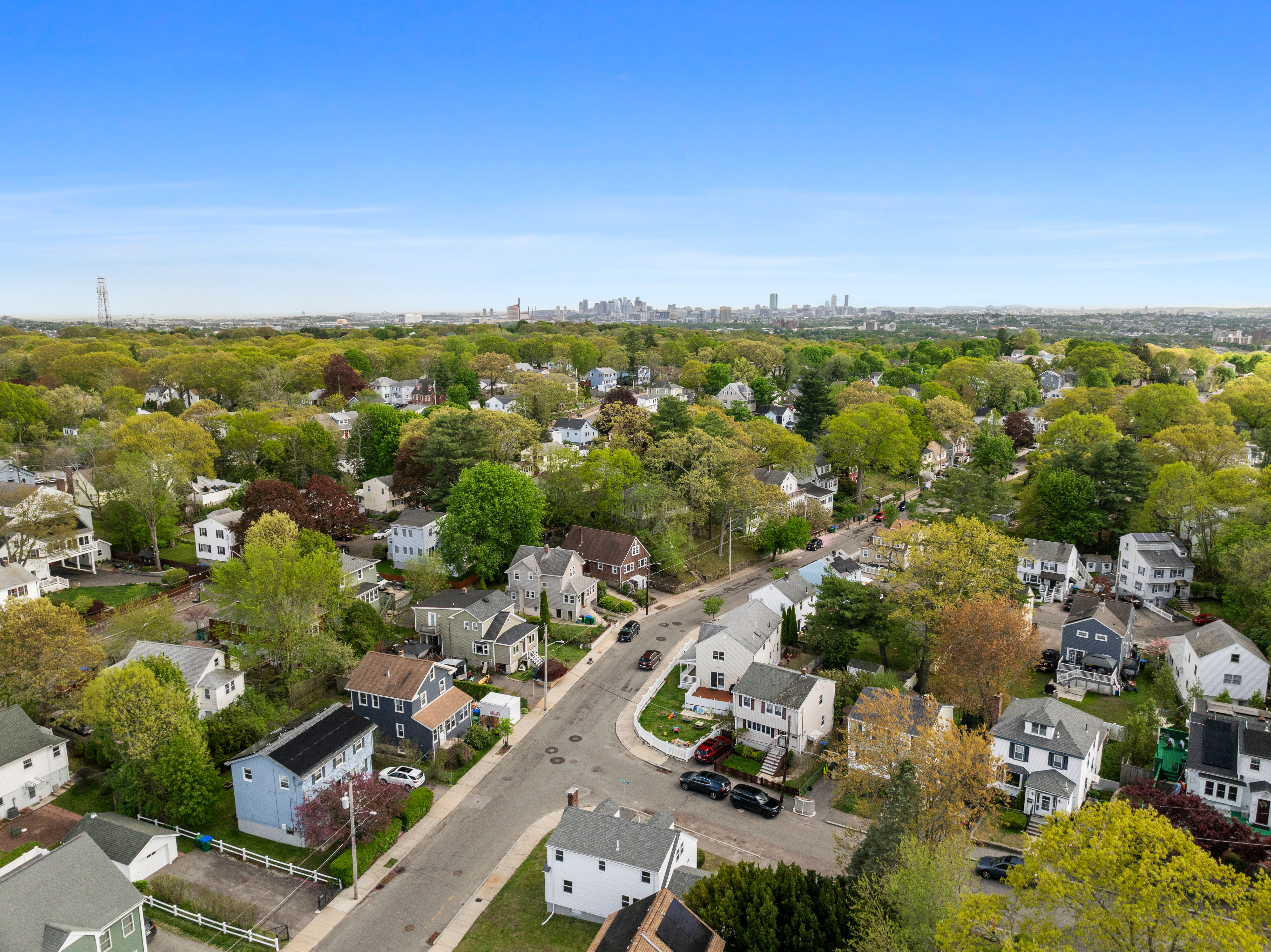 Boston suburb neighborhood with tree-lined streets and houses in the foreground, Boston skyline visible in the background