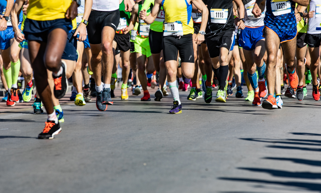A pack of runners competing in the Boston Marathon during a sunny spring day.