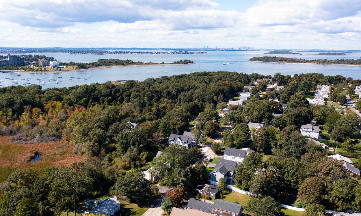 Aerial view of homes near the waterfront in Hingham, Massachusetts, with Boston Harbor and the Boston skyline in the distance.