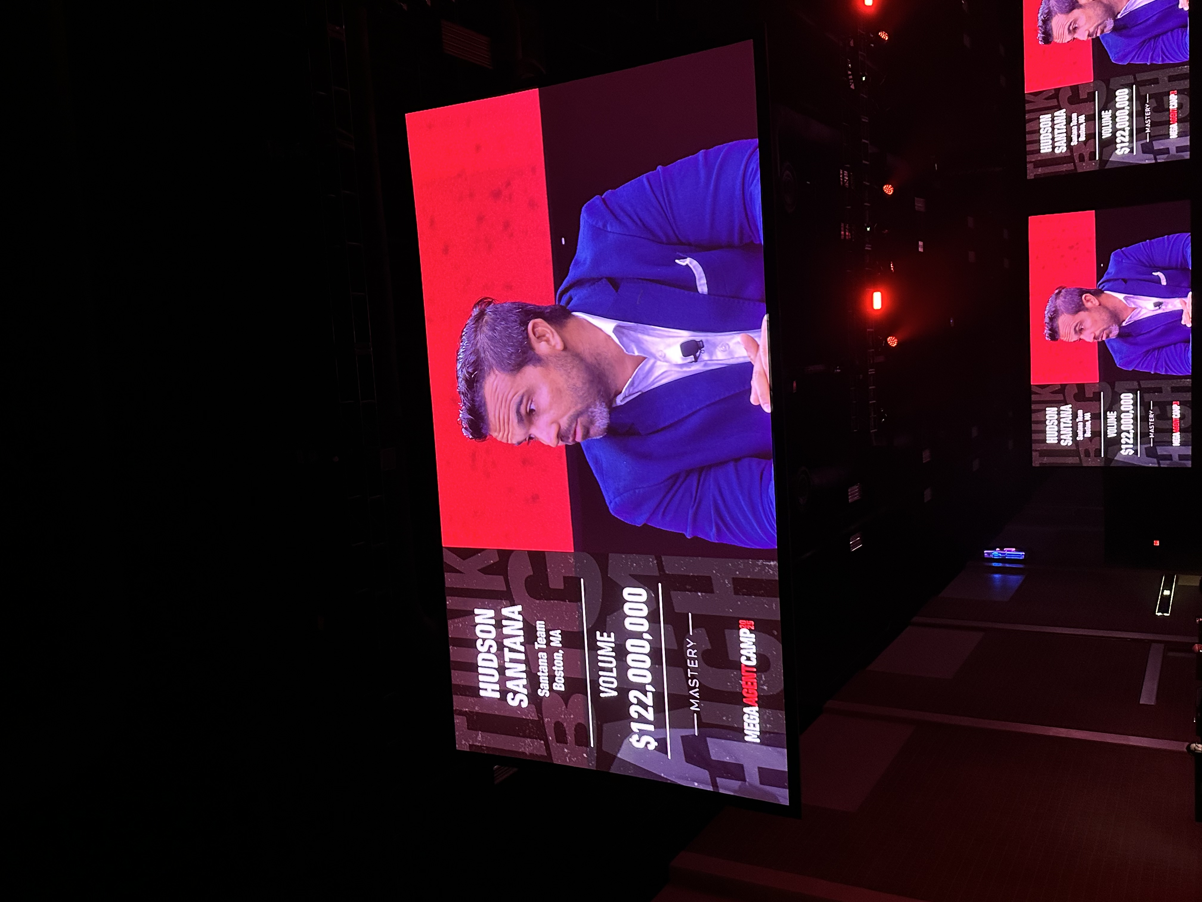 Big screen showing Hudson Santana, Santana Team, Boston MA, and volume of 122 million dollars at Mega Agent Camp