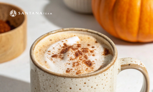 Pumpkin spice latte in a ceramic mug with cinnamon topping and a pumpkin in the background, branded with Santana Team logo