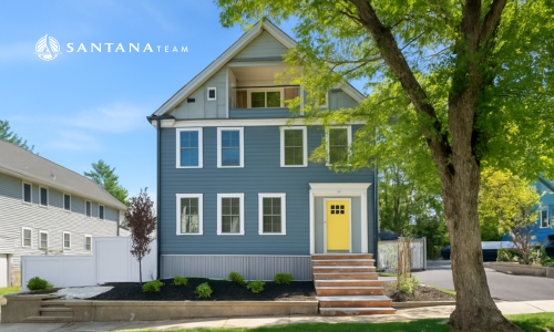 Front view of a renovated two-family home at 14 & 16 Burton Street in Arlington, Massachusetts, with blue siding, white trim, and a yellow front door, framed by a large tree.