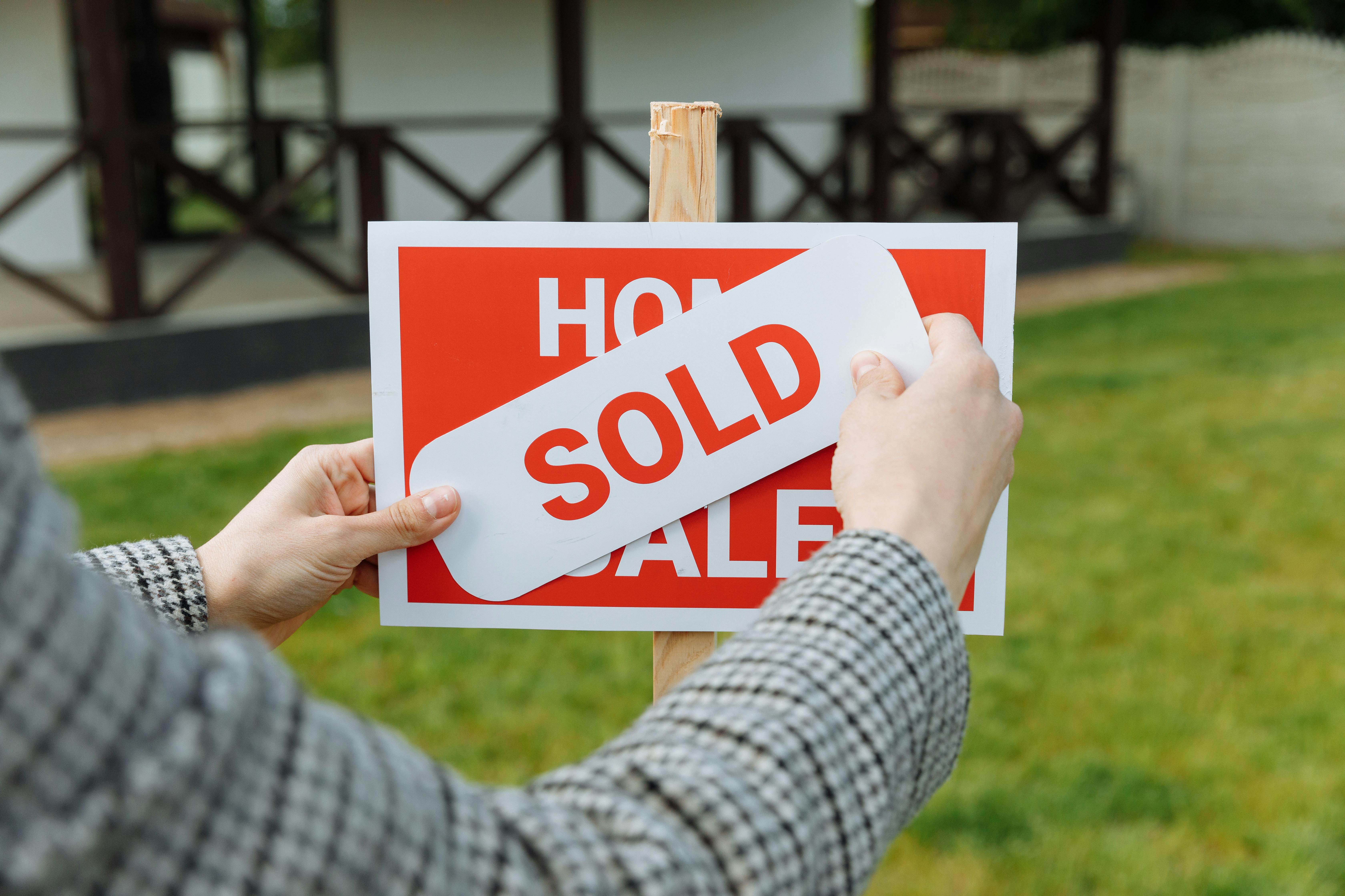 A woman placing a sold marker on a for sale sign.